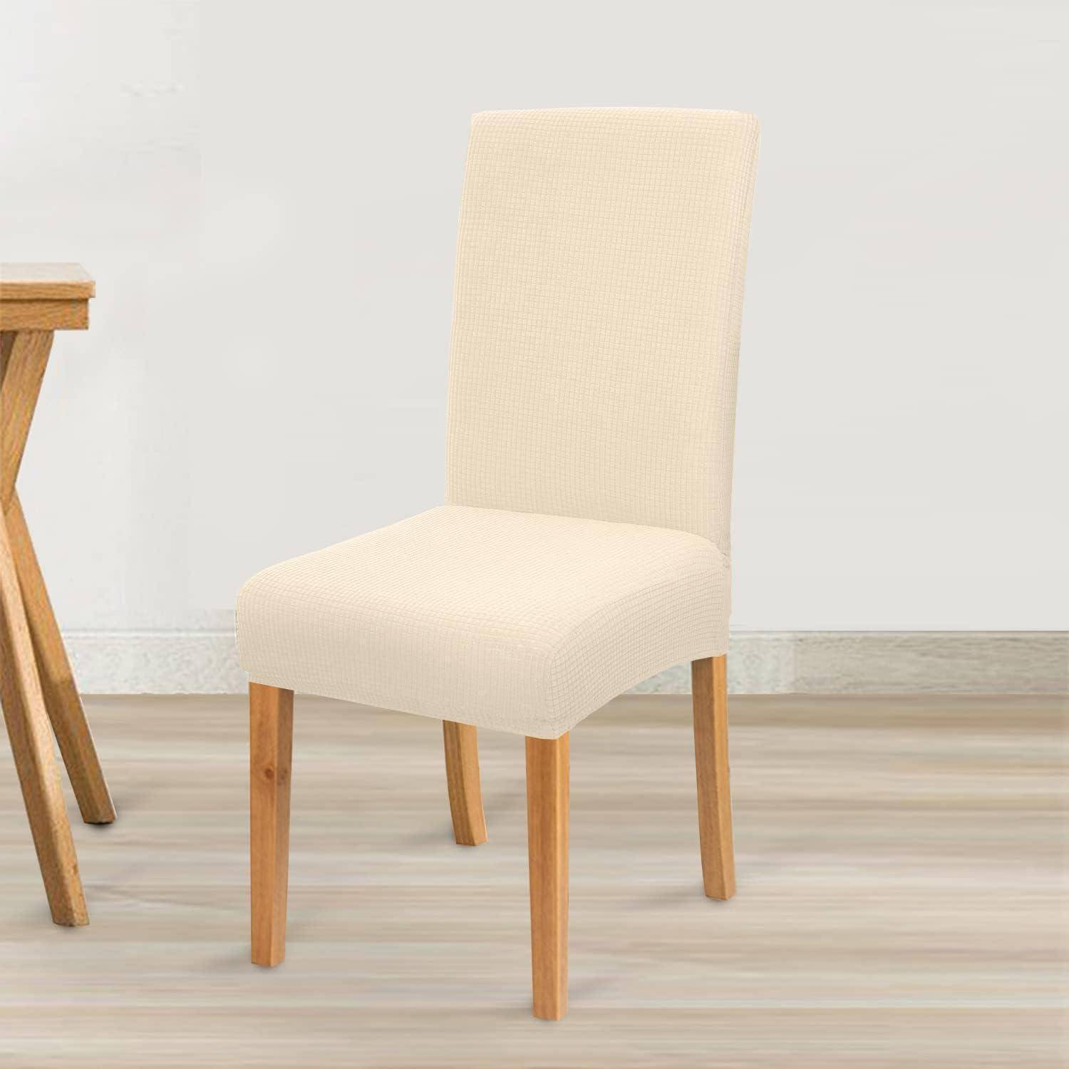 Ein beiger Stoffessstuhl mit Holzbeinen neben einem Holztisch auf einem hellen Holzboden vor einer schlichten Wand.