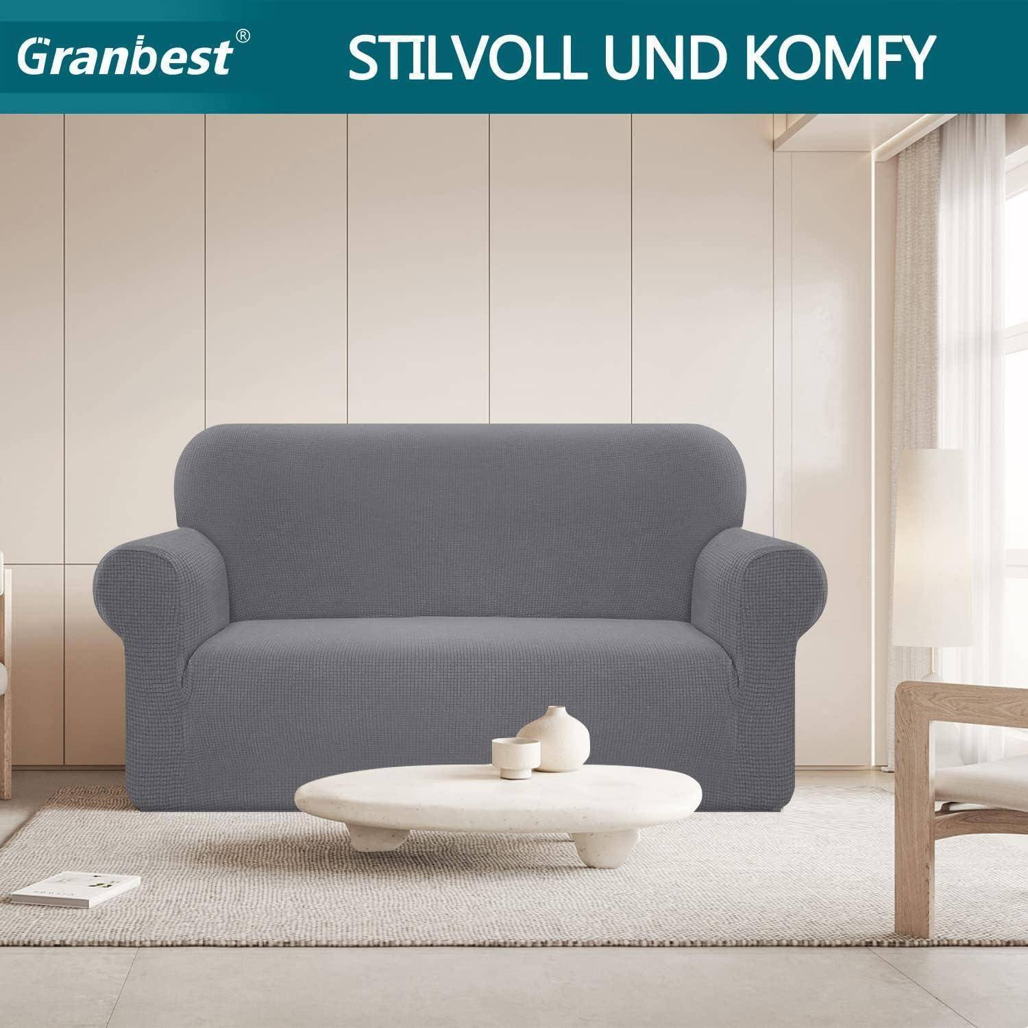 Ein grauer Sofa mit einem strukturierten Bezug befindet sich in einem modernen Wohnzimmer-Ambiente, begleitet von einem runden Couchtisch. Text lautet: 'STILVOLL UND KOMFY'.