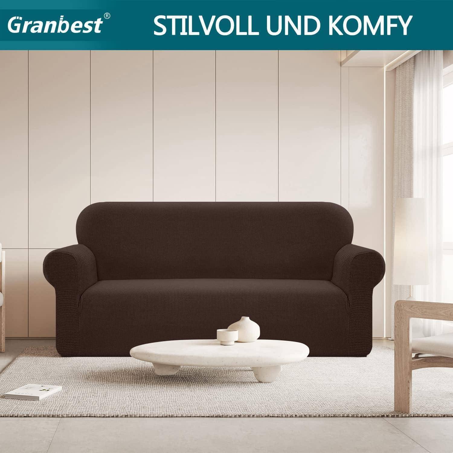Ein moderner Wohnraum mit einem dunkelbraunen Sofa, beigen Wänden und einem großen Fenster auf der rechten Seite. Text oben liest sich: 'Granbest Stilvoll und Komfy'.