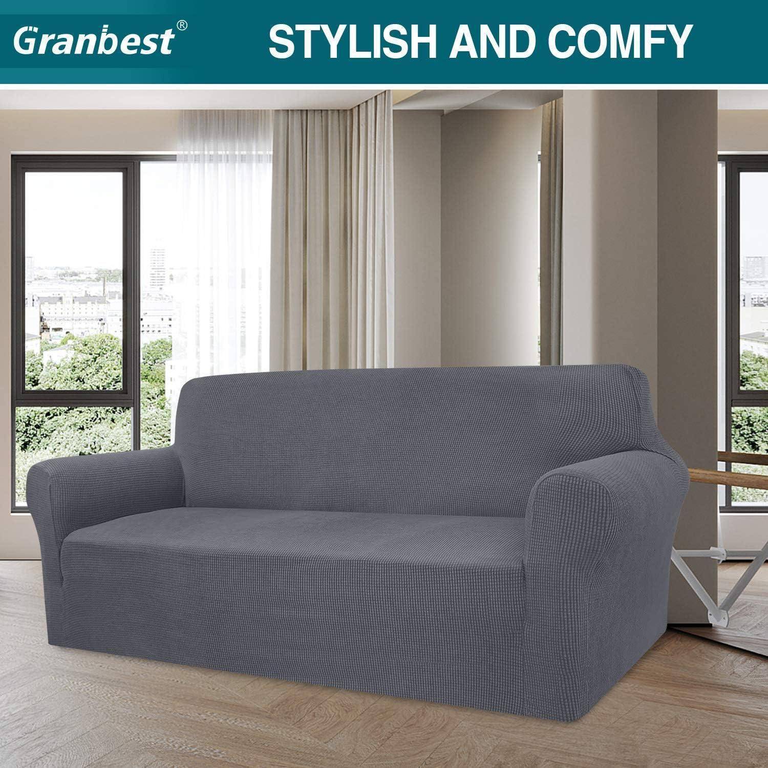 Graues Sofa mit maßgeschneiderter Husse in einem modernen Wohnzimmer. Große Fenster mit Vorhängen lassen natürliches Licht herein. Text lautet: 
