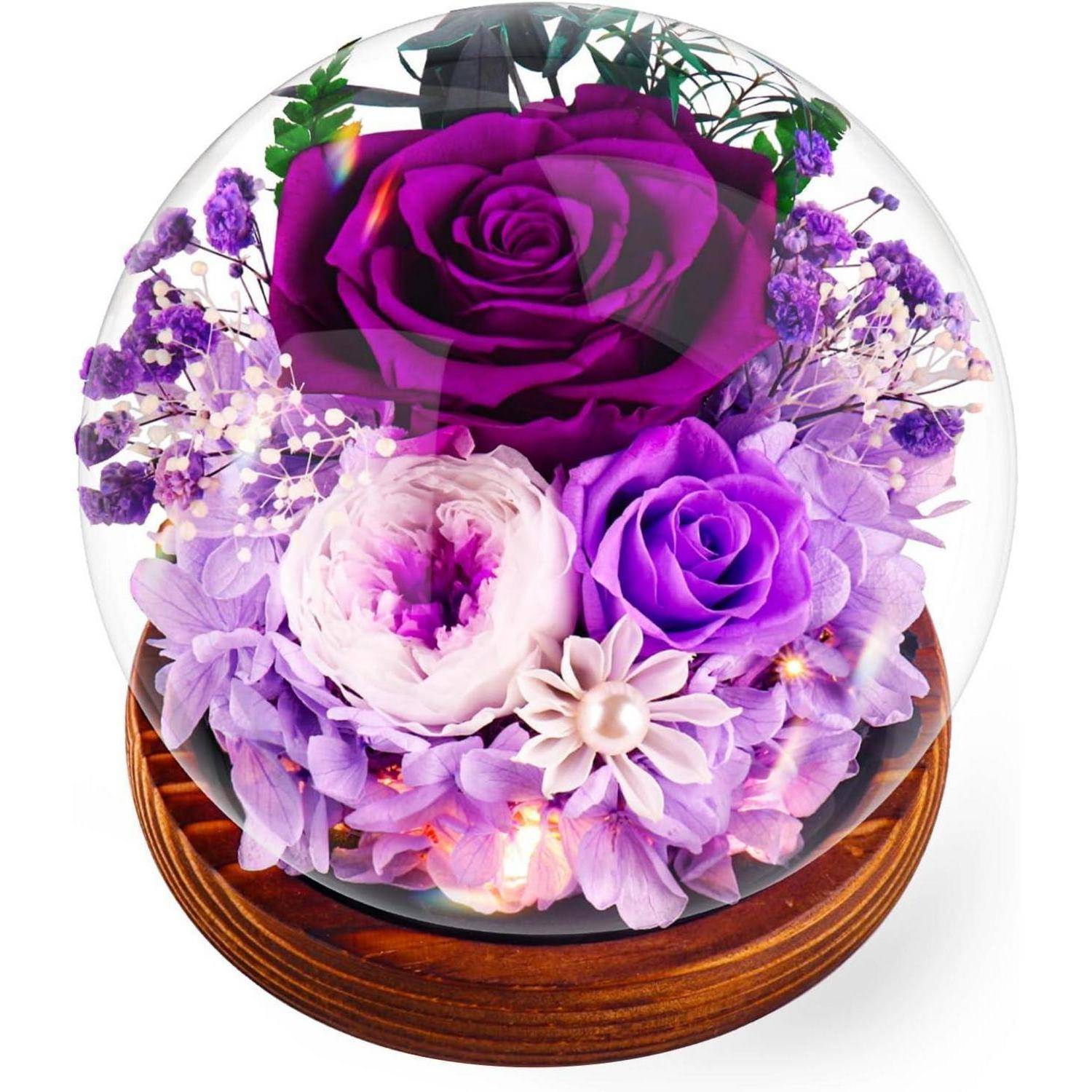 Ein konserviertes Blumenarrangement in einer Glaskuppel mit violetten Rosen und Lavendelblüten auf einer Holzbasis.
