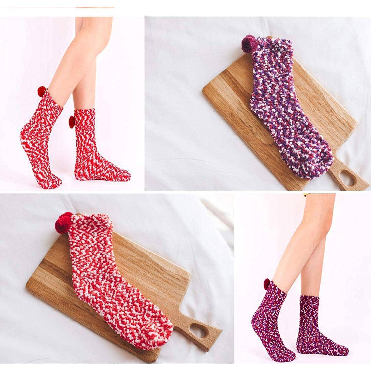 Bunte gestrickte Socken mit Pompons werden auf einem Holzbrett ausgelegt und von einer Person getragen. Zwei Paare werden gezeigt: rote und lila Designs.