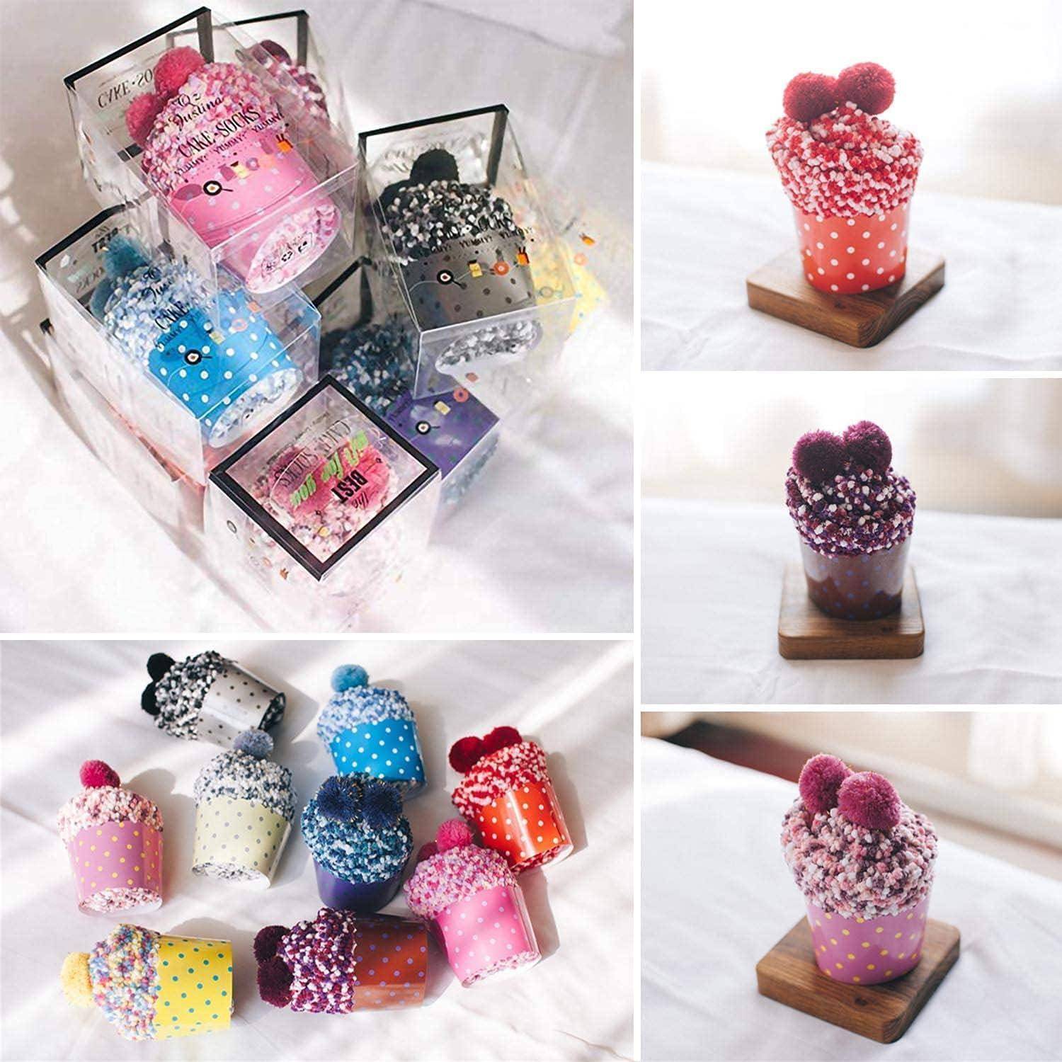 Verschiedene Cupcake-Handtücher mit Polka-Dots, in Geschenkboxen auf Holzablagen präsentiert, jedes Handtuch mit Pompons in unterschiedlichen Farben verziert.