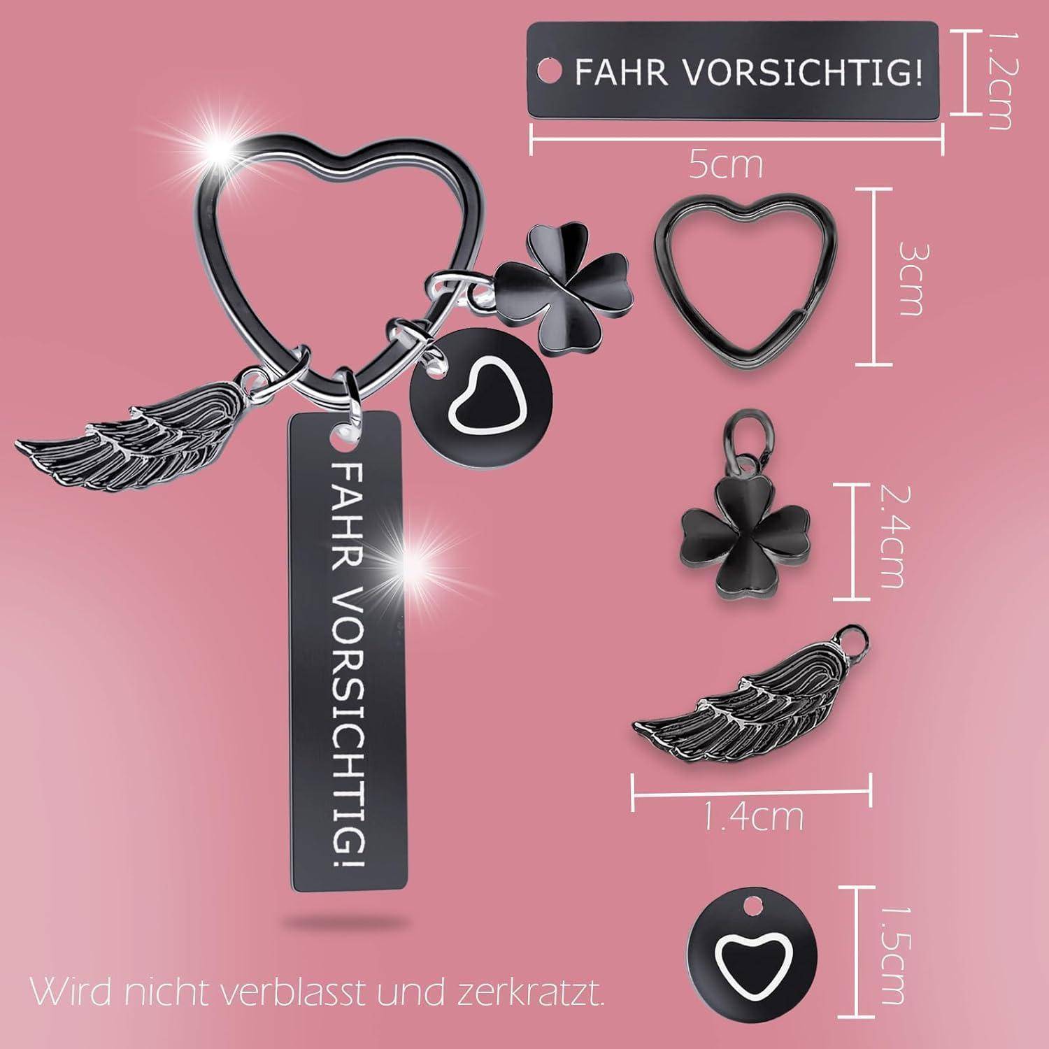 Schlüsselanhänger-Set mit schwarzem rechteckigem Anhänger mit der Aufschrift 'FAHR VORSICHTIG!', Herzring, Kleeblatt, Flügel, Herz-Charm. Verschiedene Größen dargestellt.