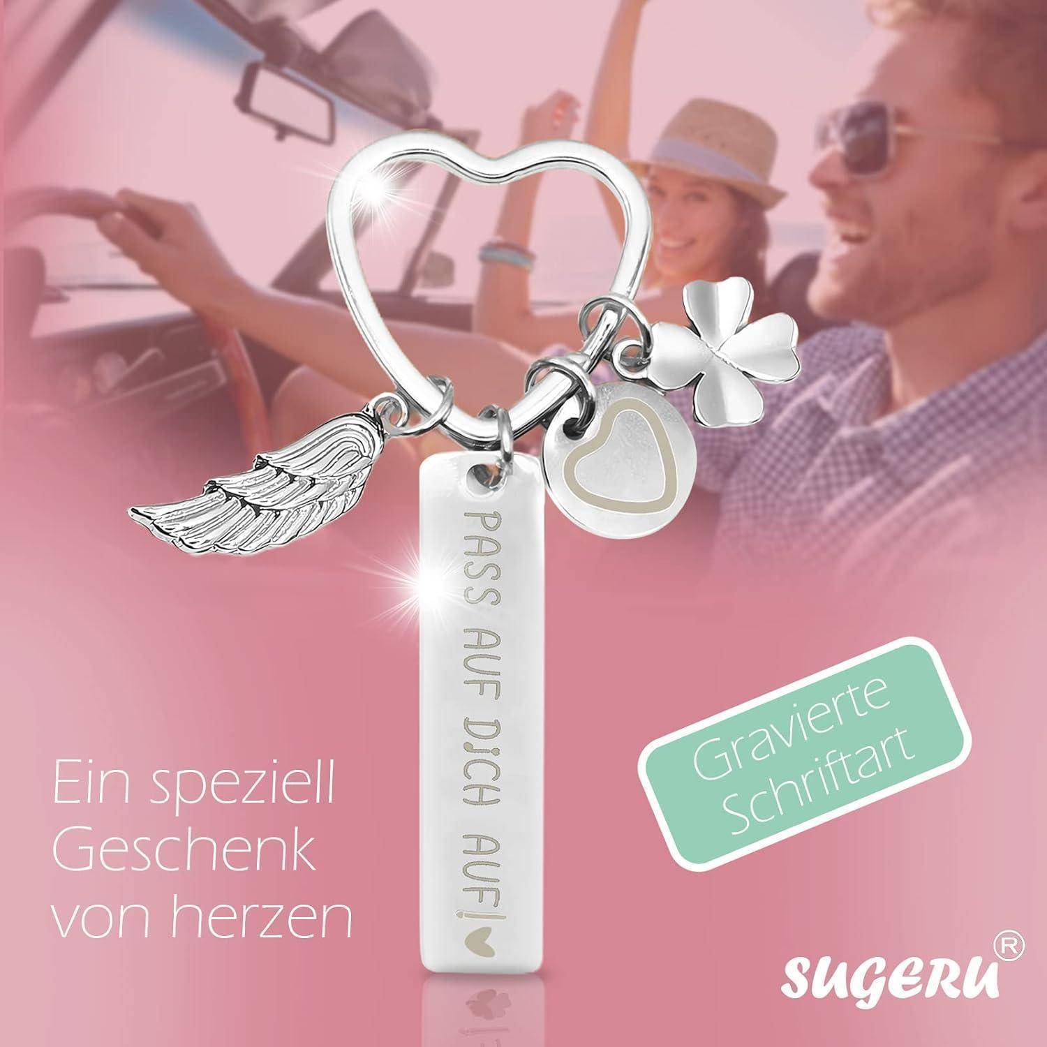 Ein Schlüsselanhänger mit einem Herzen und Anhängern mit dem Text 'PASS AUF DICH AUF' und einem Glücksklee. Im Hintergrund sitzt ein Paar in einem Auto.