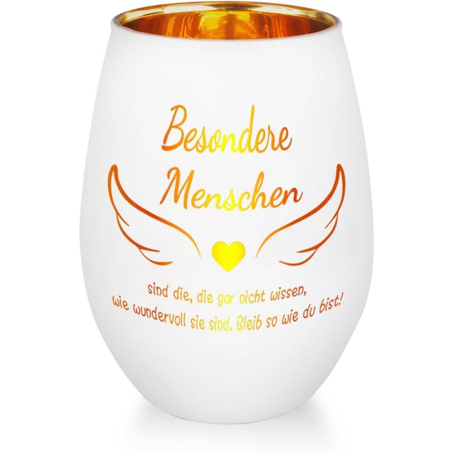 Ein weißer Kerzenhalter mit goldener Innenseite trägt den Text 'Besondere Menschen sind die, die gar nicht wissen, wie wundervoll sie sind. Bleib so wie du bist!' mit dekorativen Flügeln und einem Herzdesign.