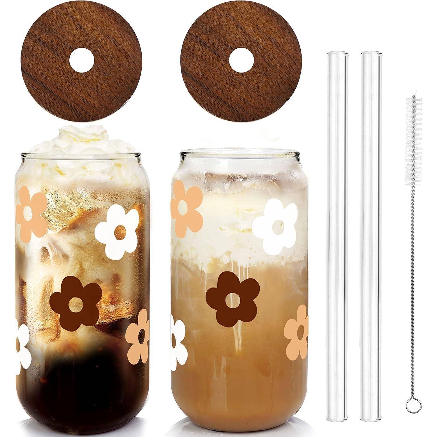 Zwei Trinkgläser mit Blumenmuster und Holzdeckeln, gefüllt mit Eiskaffee und cremiger Schaumkrone, daneben zwei durchsichtige Strohhalme und eine Reinigungsbürste.
