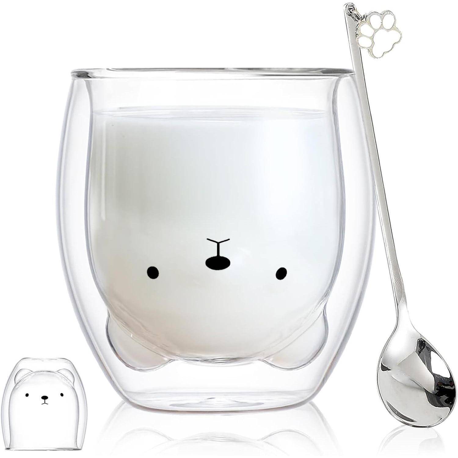 Eine transparente Tasse mit einem süßen Bärchen-Gesicht-Design, gefüllt mit Milch, neben einem Löffel mit einem Bärentatzen-Aufdruck am Griff.