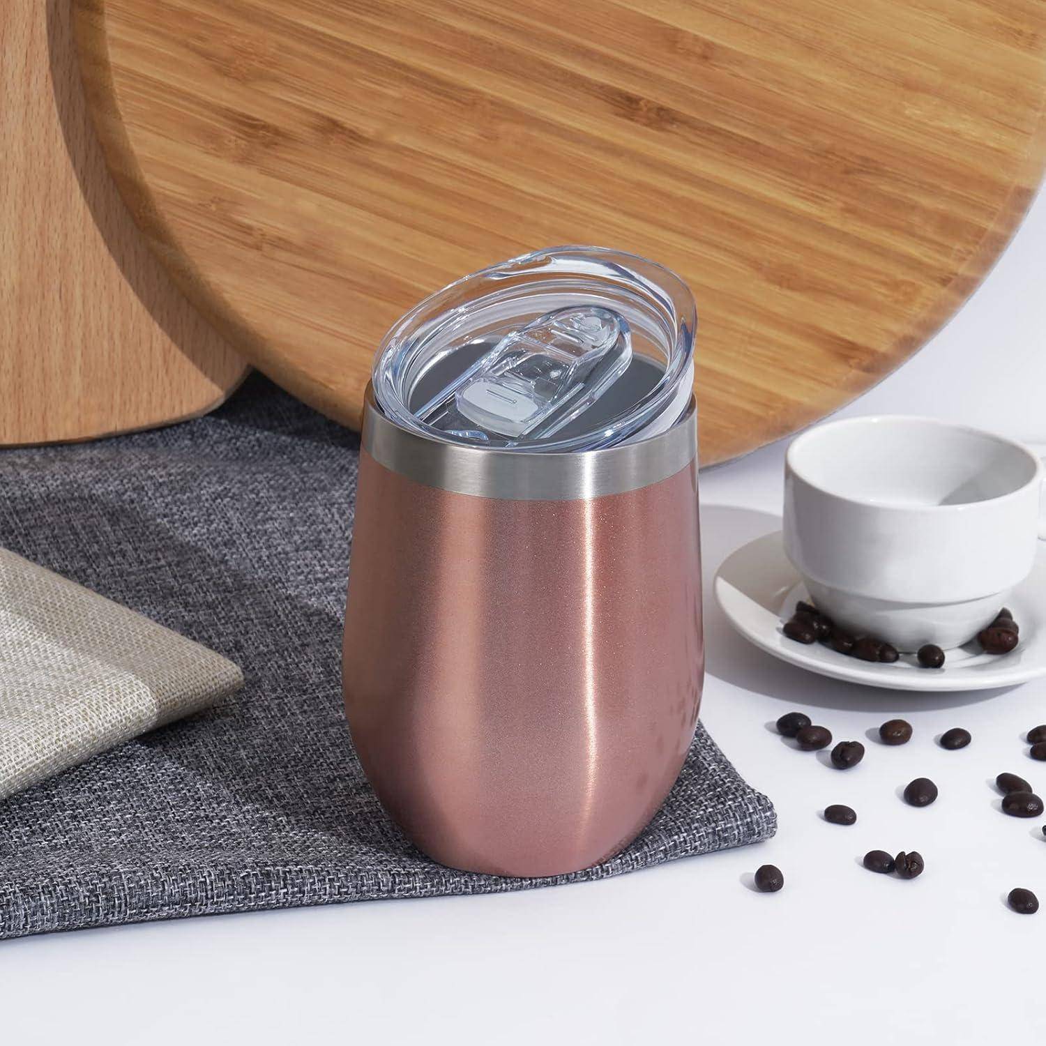 Ein Isolierbecher aus Edelstahl mit Deckel liegt auf einer grauen Matte, daneben ein Holzschneidebrett, eine weiße Tasse und verstreute Kaffeebohnen.