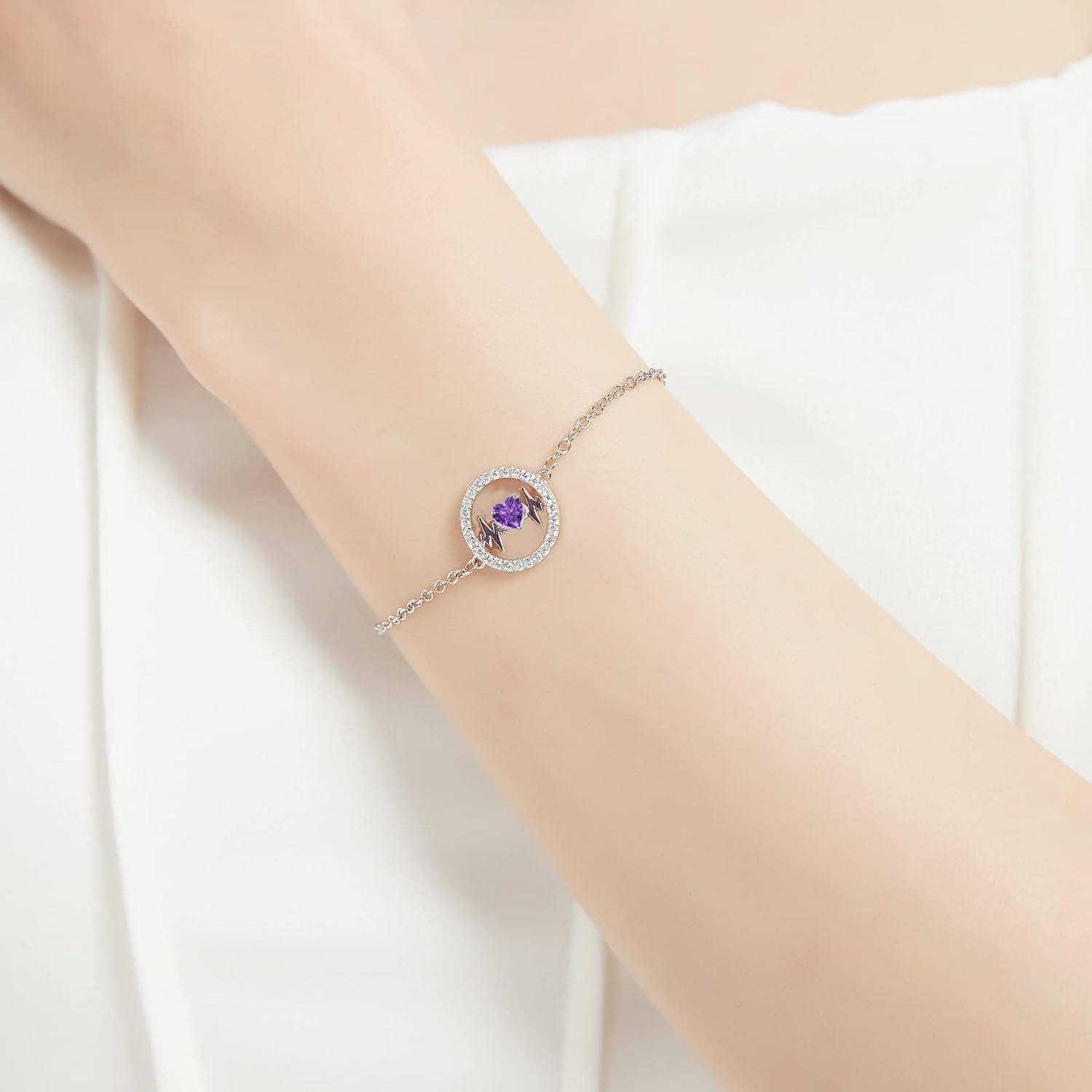 Ein zarter Armreif wird am Handgelenk getragen, der ein kreisförmiges Design mit einem zentralen violetten Edelstein aufweist, der von kleinen klaren Steinen umgeben ist.