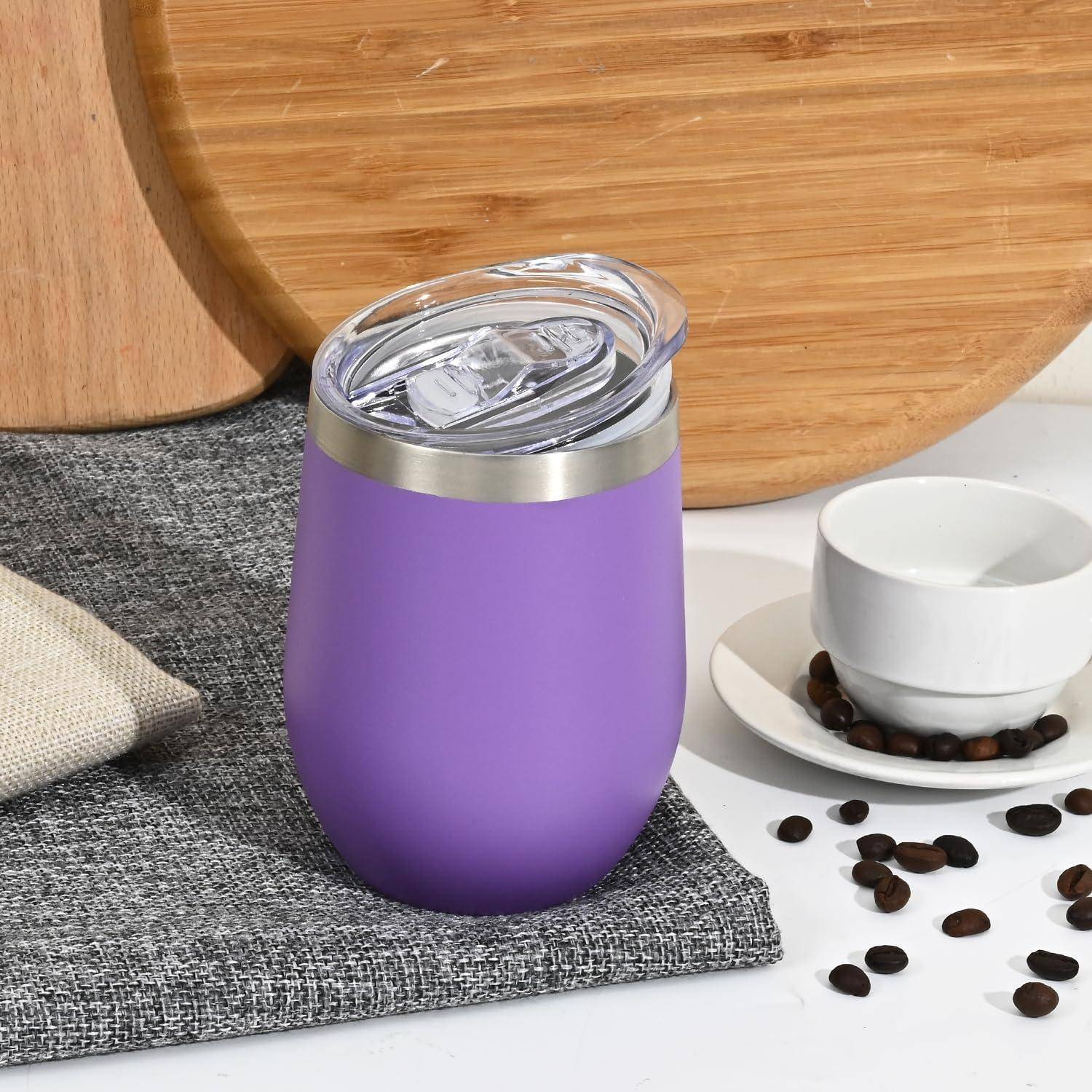 Ein lila isolierter Thermobecher mit einem durchsichtigen Deckel steht auf einem grauen Platzdeckchen neben einer kleinen weißen Tasse und verstreuten Kaffeebohnen.