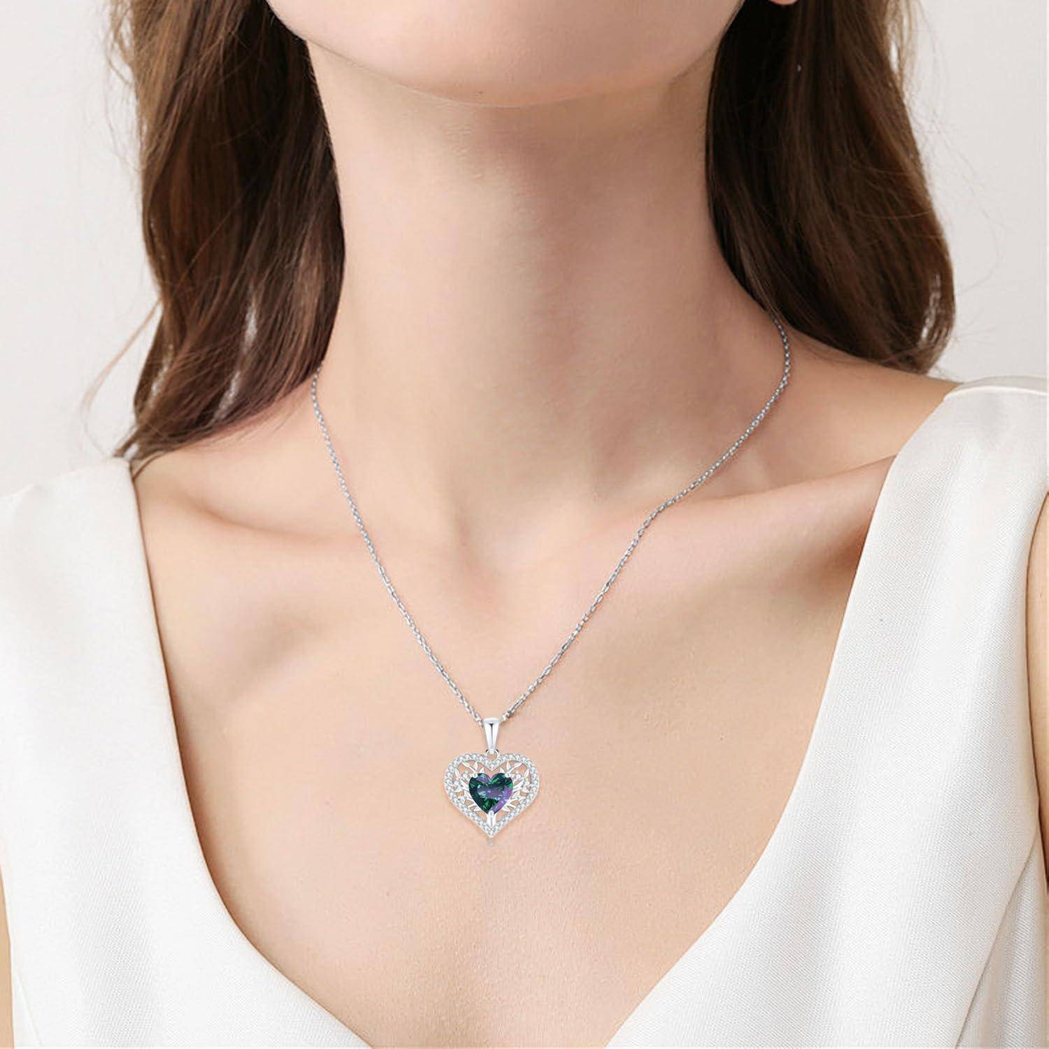 Eine Person, die ein weißes Oberteil und eine silberne Halskette mit einem herzförmigen blauen Anhänger trägt und damit Eleganz und Stil unterstreicht.