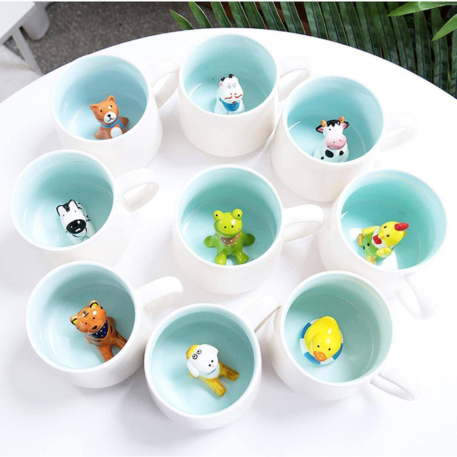 Neun weiße Tassen, die in einem Kreis angeordnet sind, wobei jede eine kleine Tierfigur im Inneren enthält, auf einer weißen Oberfläche mit grünen Blättern in der Nähe.