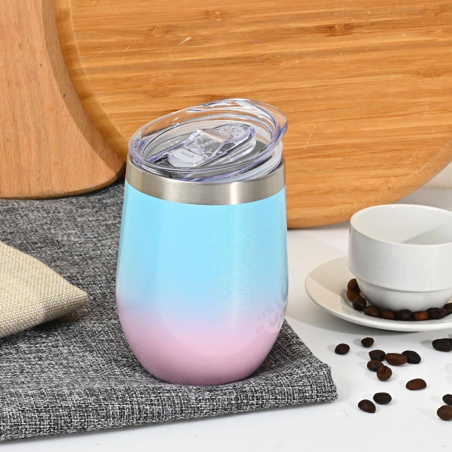 Eine metallische Rosa-zu-Blau-Verlaufstasse mit einem durchsichtigen Deckel steht auf einer grauen Stoffoberfläche, umgeben von Kaffeebohnen und einer Tasse.