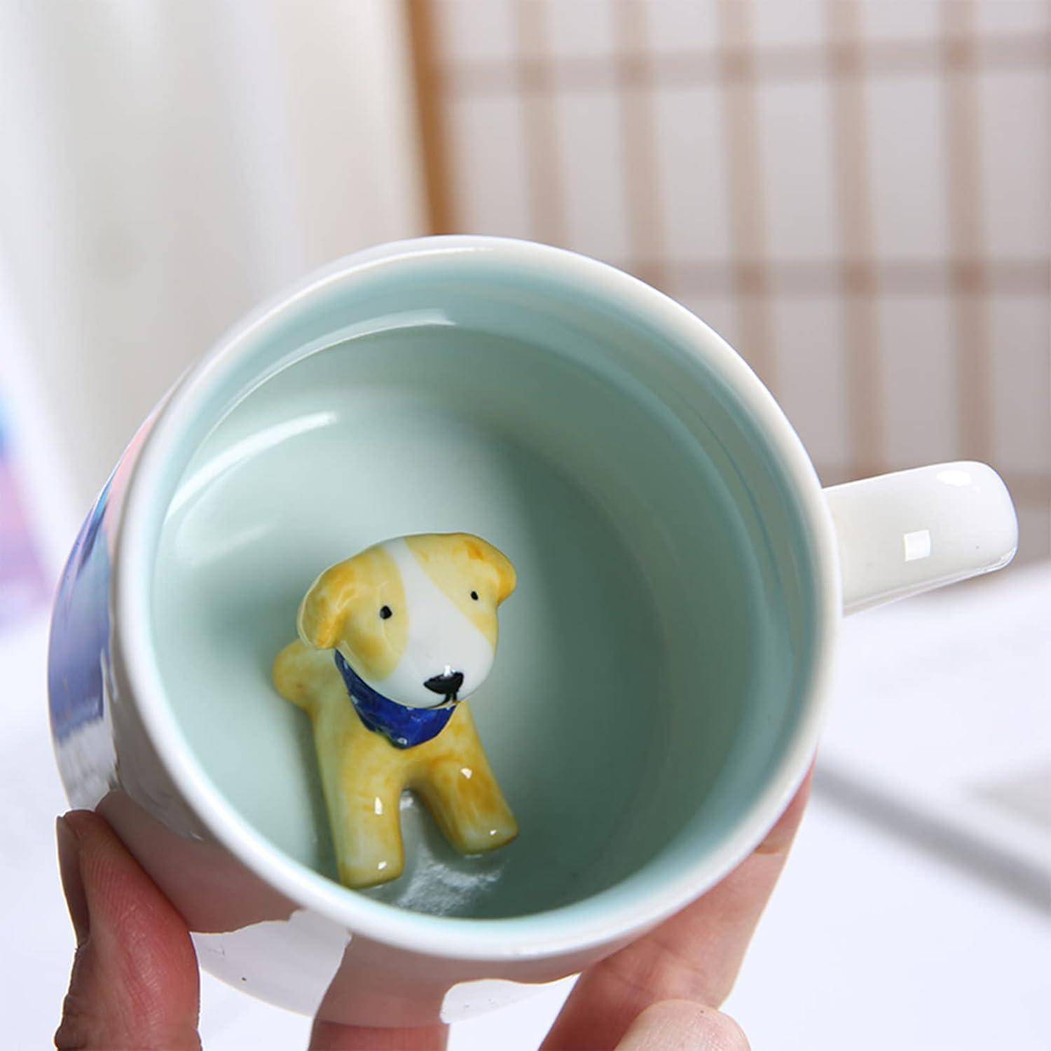 Eine Hand, die eine Tasse hält, aus deren Boden innen eine keramische Hundefigur herausragt und so ein verspieltes Überraschungselement schafft.