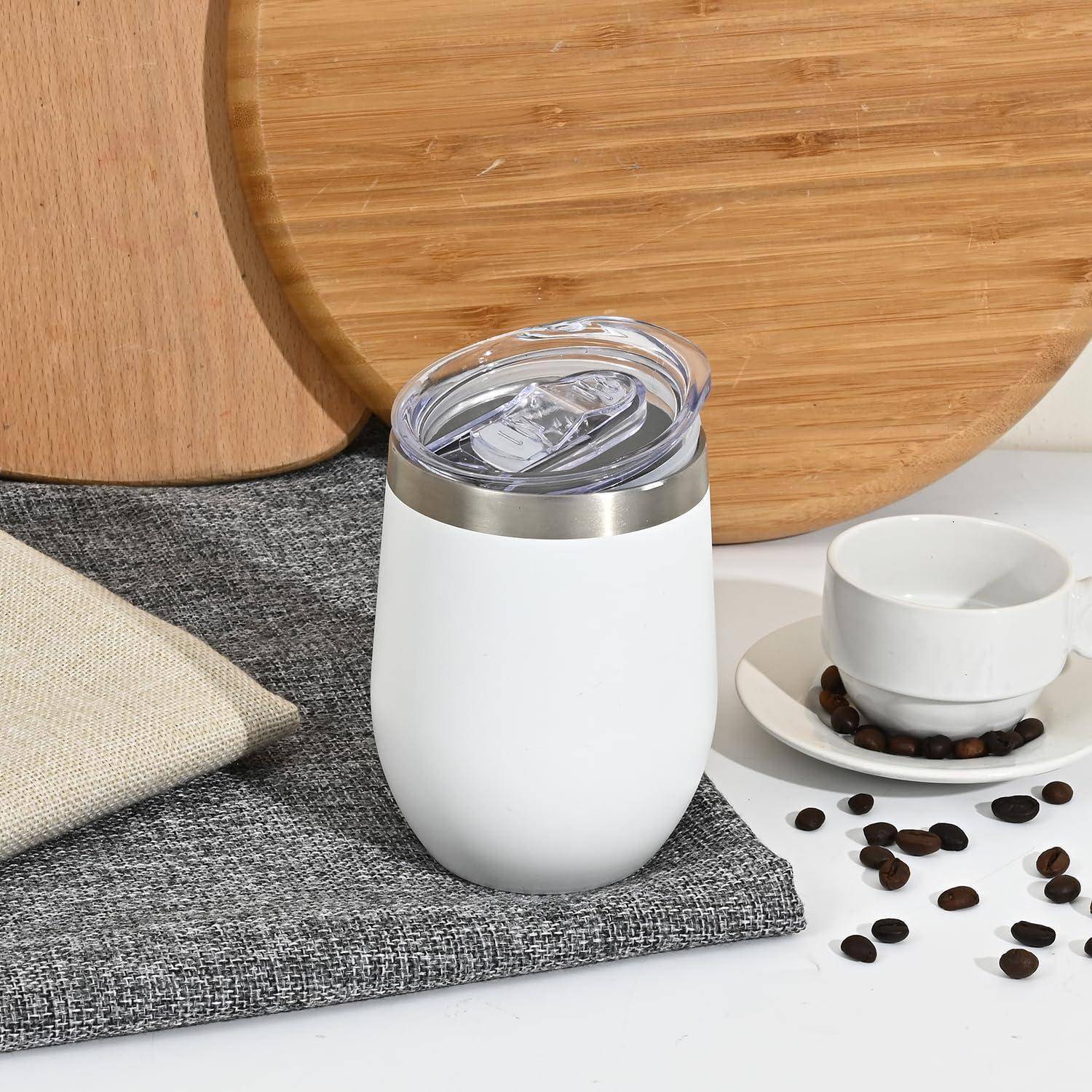 Ein weißer isolierter Becher mit einem durchsichtigen Deckel steht auf einer grauen Serviette neben einer weißen Kaffeetasse und Untertasse, umgeben von Kaffeebohnen.