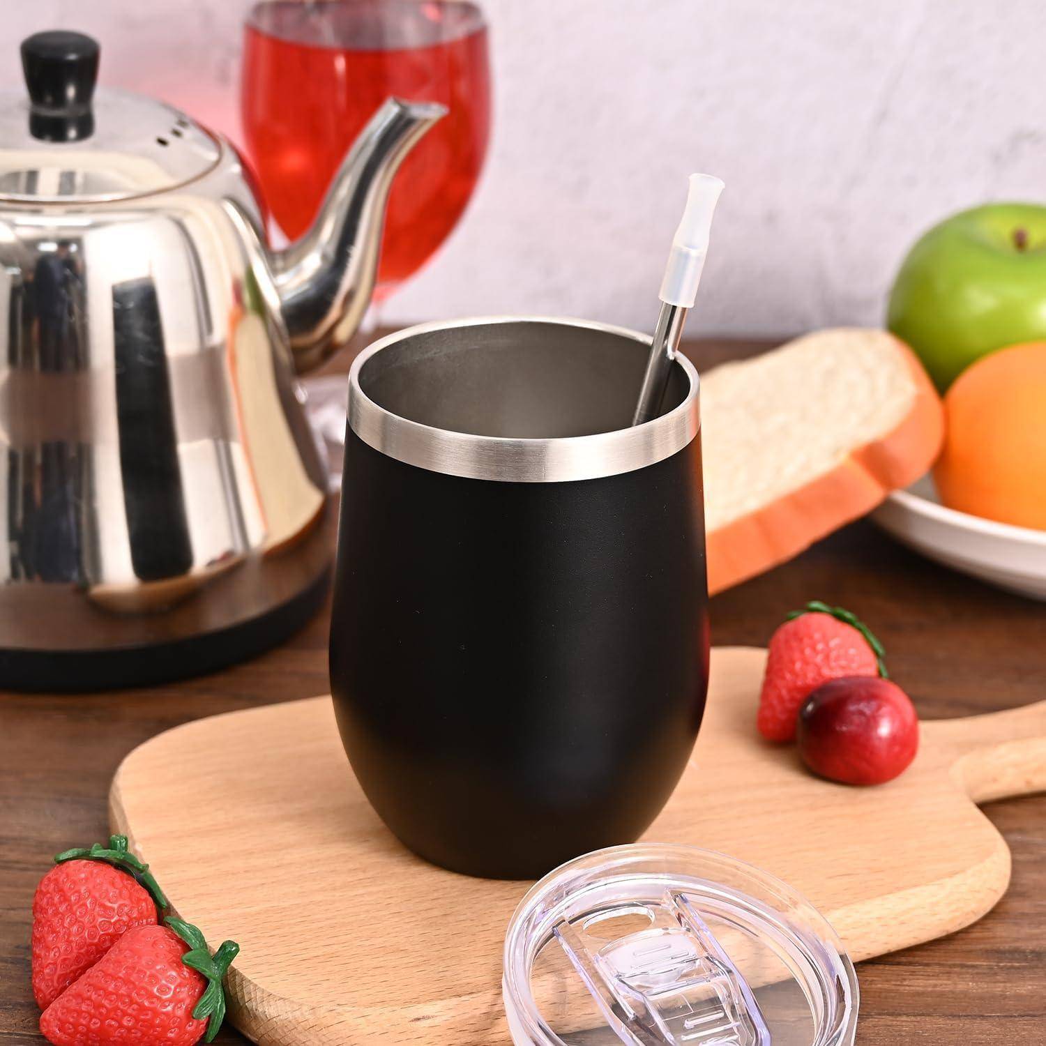 Eine schwarze isolierte Tasse mit einem Metallstrohhalm auf einem Holzbrett, umgeben von frischen Erdbeeren, einem Apfel, einem Sandwich und einem Glas rotem Saft.