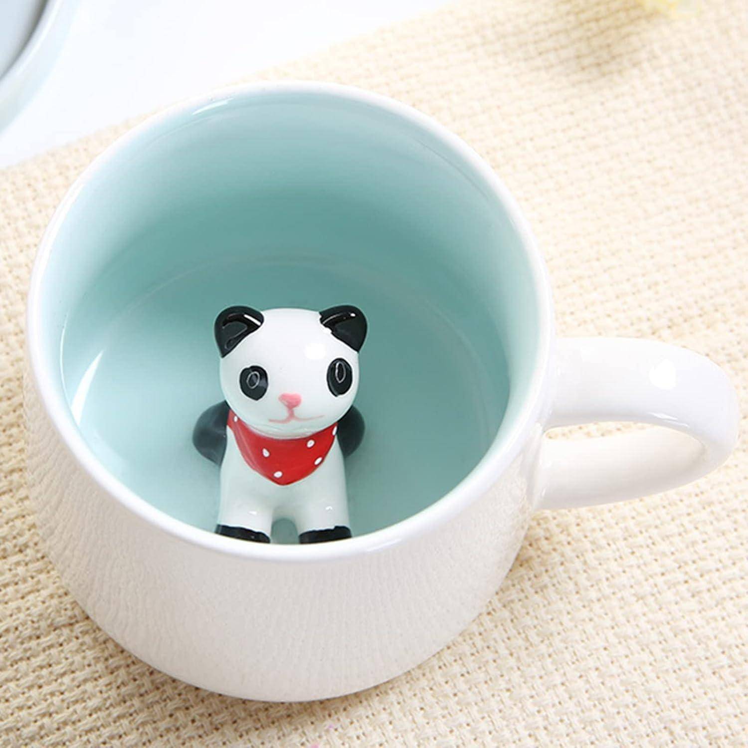 Eine weiße Tasse mit hellblauem Innenraum zeigt einen kleinen Keramik-Panda, der einen roten Schal trägt und am unteren Rand innen positioniert ist.