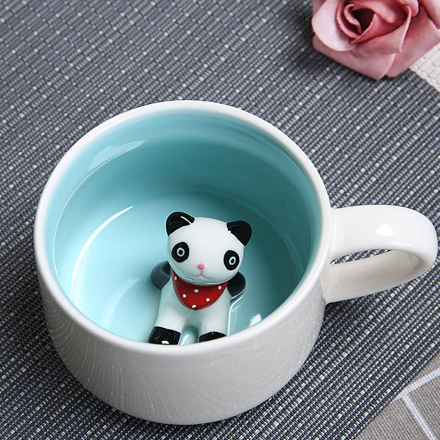 Eine kleine Pandafigur sitzt in einer blau-weißen Tasse, daneben liegt eine rosa Rose auf einer strukturierten grauen Oberfläche.