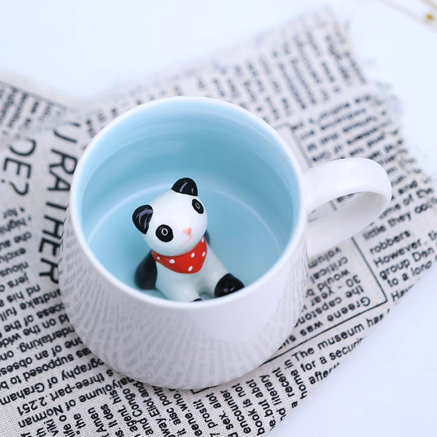 Eine Keramiktasse mit einer kleinen Pandafigur im Inneren, platziert auf einem Zeitungsstück. Der Panda trägt einen roten Polkatupfenschal.