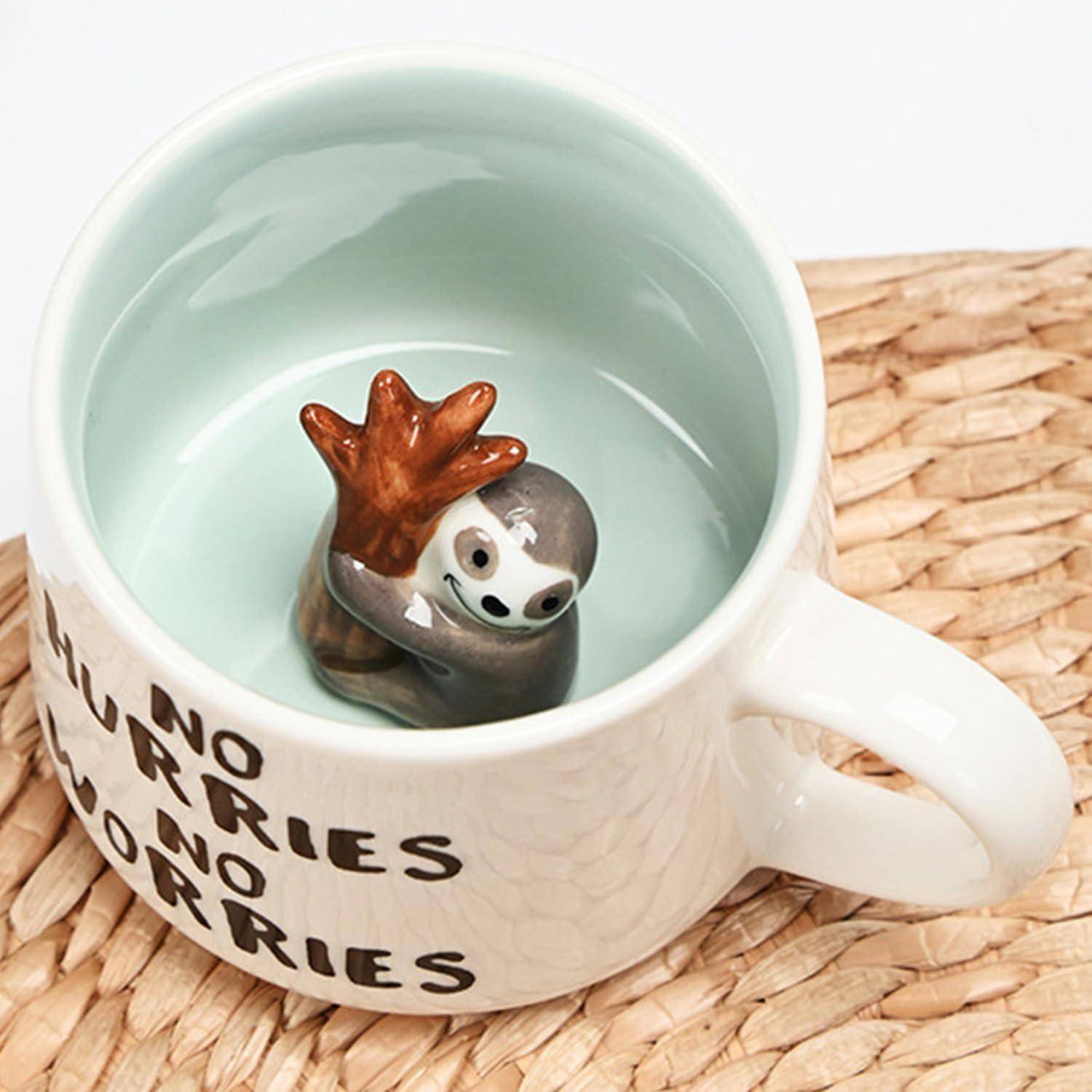 Eine Tasse auf einer geflochtenen Matte zeigt einen Keramik-Faultier, der einen Ast hält. Auf der Tasse steht: „Keine Eile, keine Sorgen.