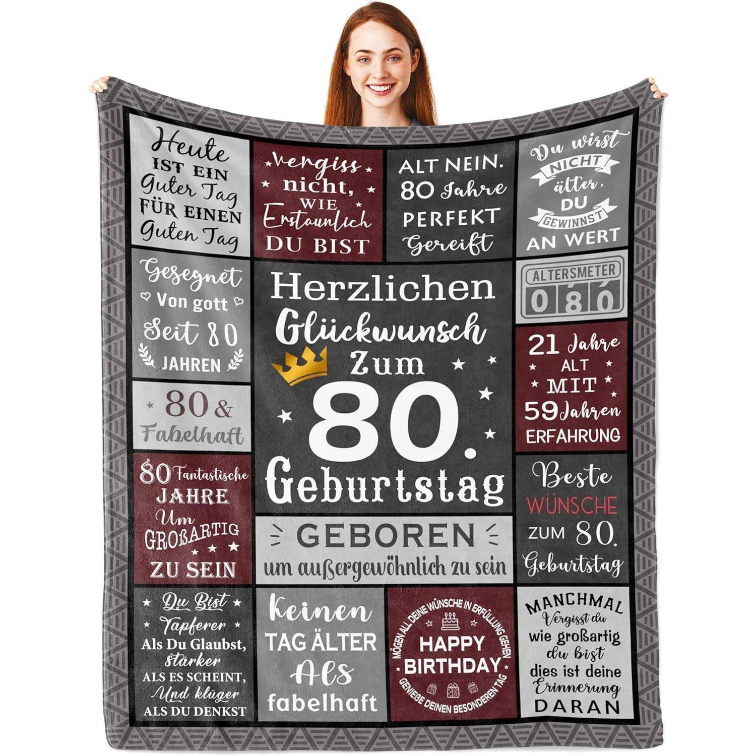 Eine Person hält eine dekorative Decke mit deutschen Geburtstagsbotschaften, die einen 80. Geburtstag feiern und verschiedene Glückwunschformeln beinhalten.