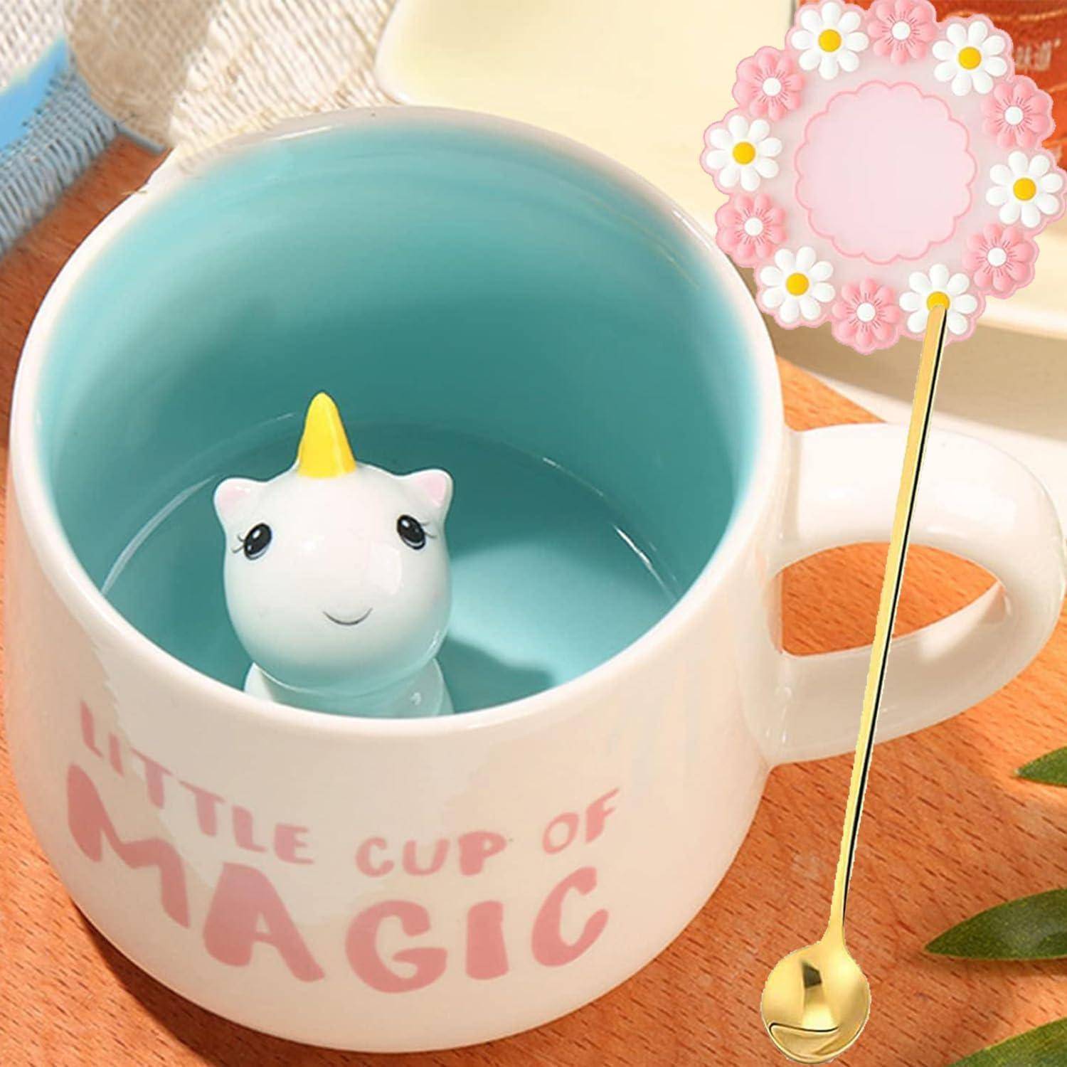 Eine Keramiktasse mit der Aufschrift 'Kleine Tasse voller Magie' und einer niedlichen Einhornfigur im Inneren. Daneben liegt ein dekorativer Löffel mit einem Blumenhenkel.