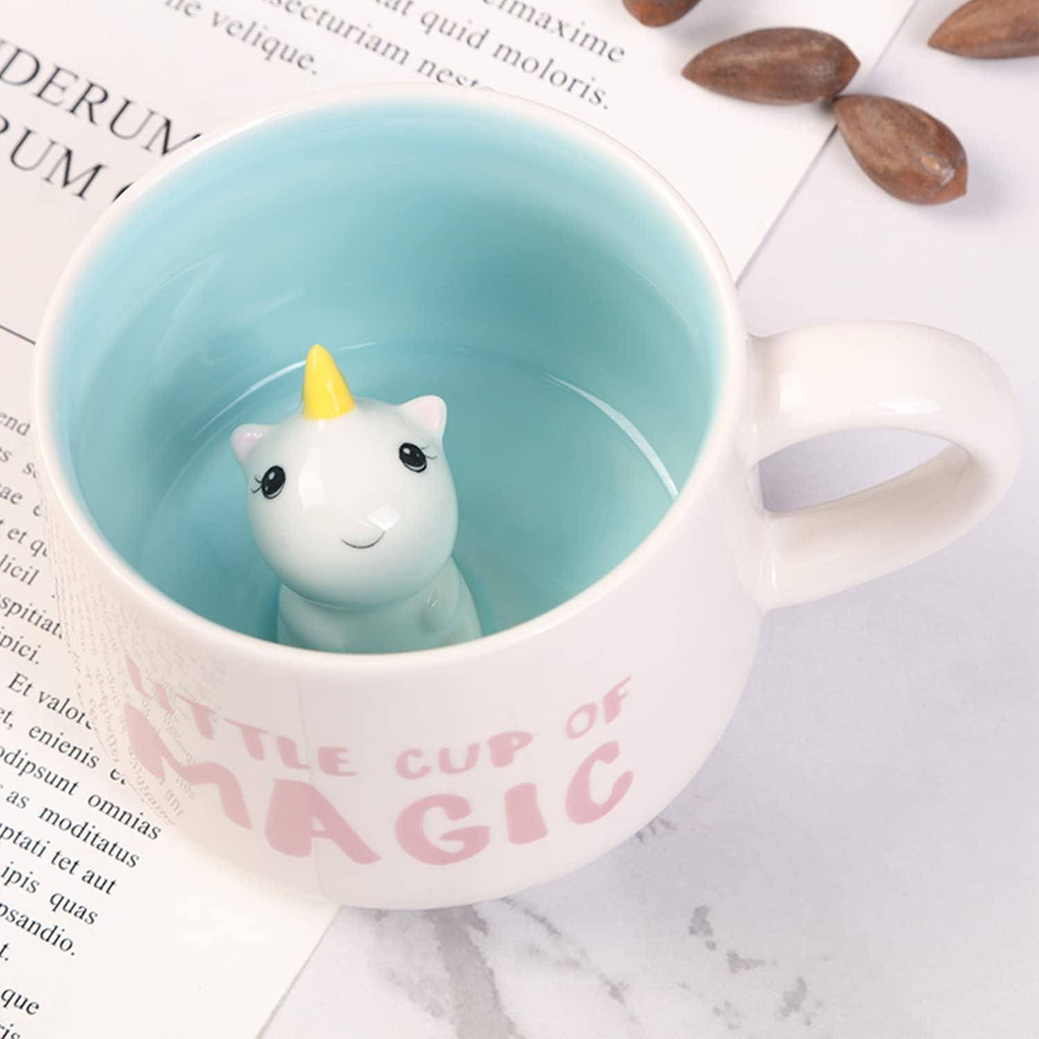 Eine weiße Tasse mit blauer Innenseite, die eine kleine Einhornfigur im Inneren enthält. Die Tasse trägt die Aufschrift 