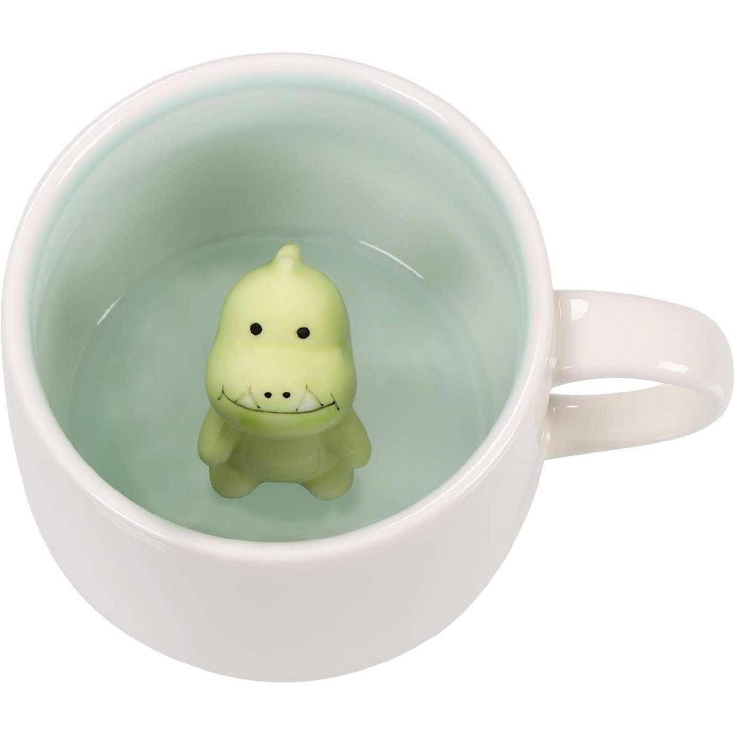 Eine weiße Tasse enthält eine blassgrüne Dinosaurierfigur am Boden, die den Eindruck erweckt, als würde der Dinosaurier schwimmen, wenn die Tasse gefüllt wird.