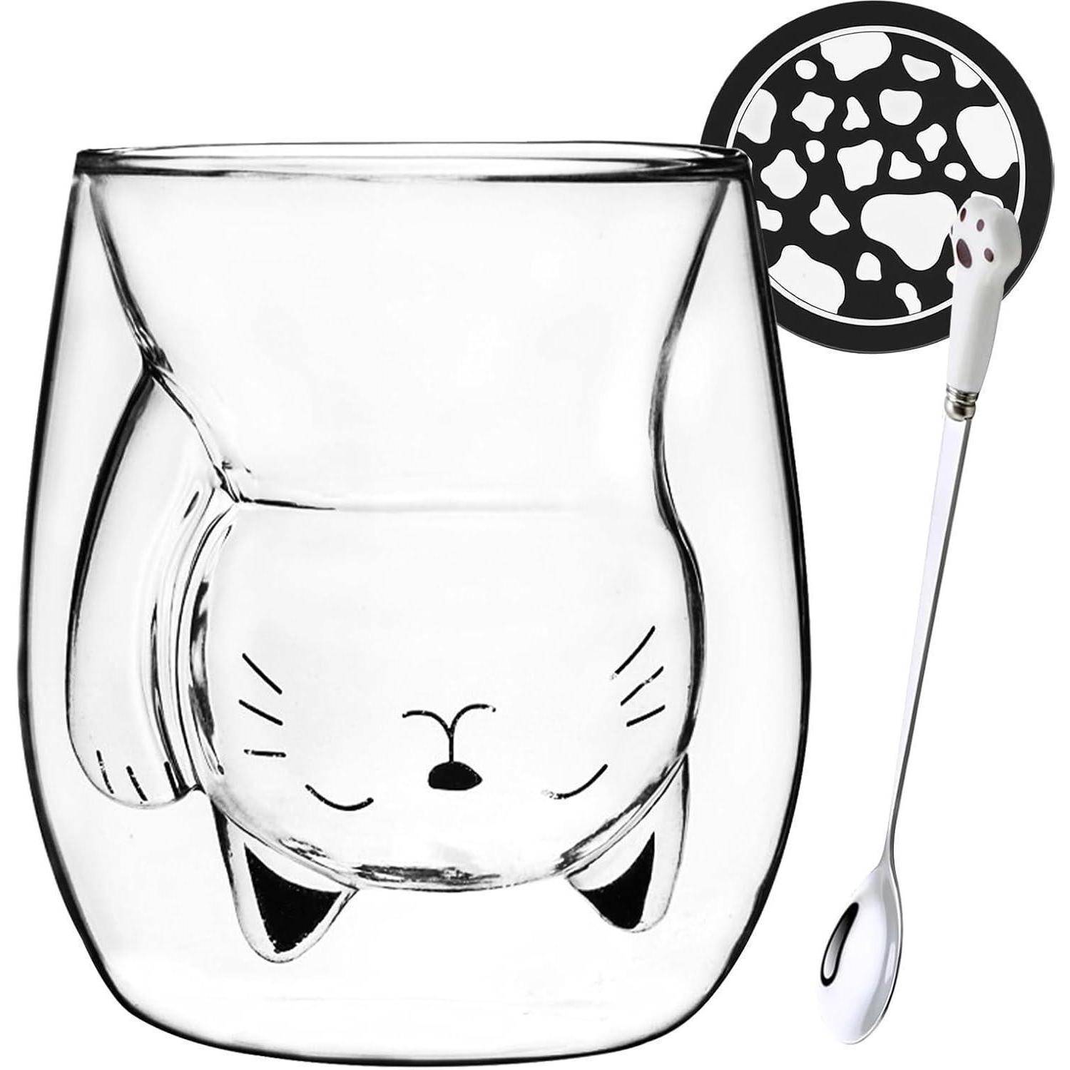 Eine klare Glasstasse mit einem auf den Kopf gestellten Katzenkopf, der ins Glas geätzt ist, kombiniert mit einem passenden katzenförmigen Löffel und einem Untersetzer mit Pfotenabdruckmuster.