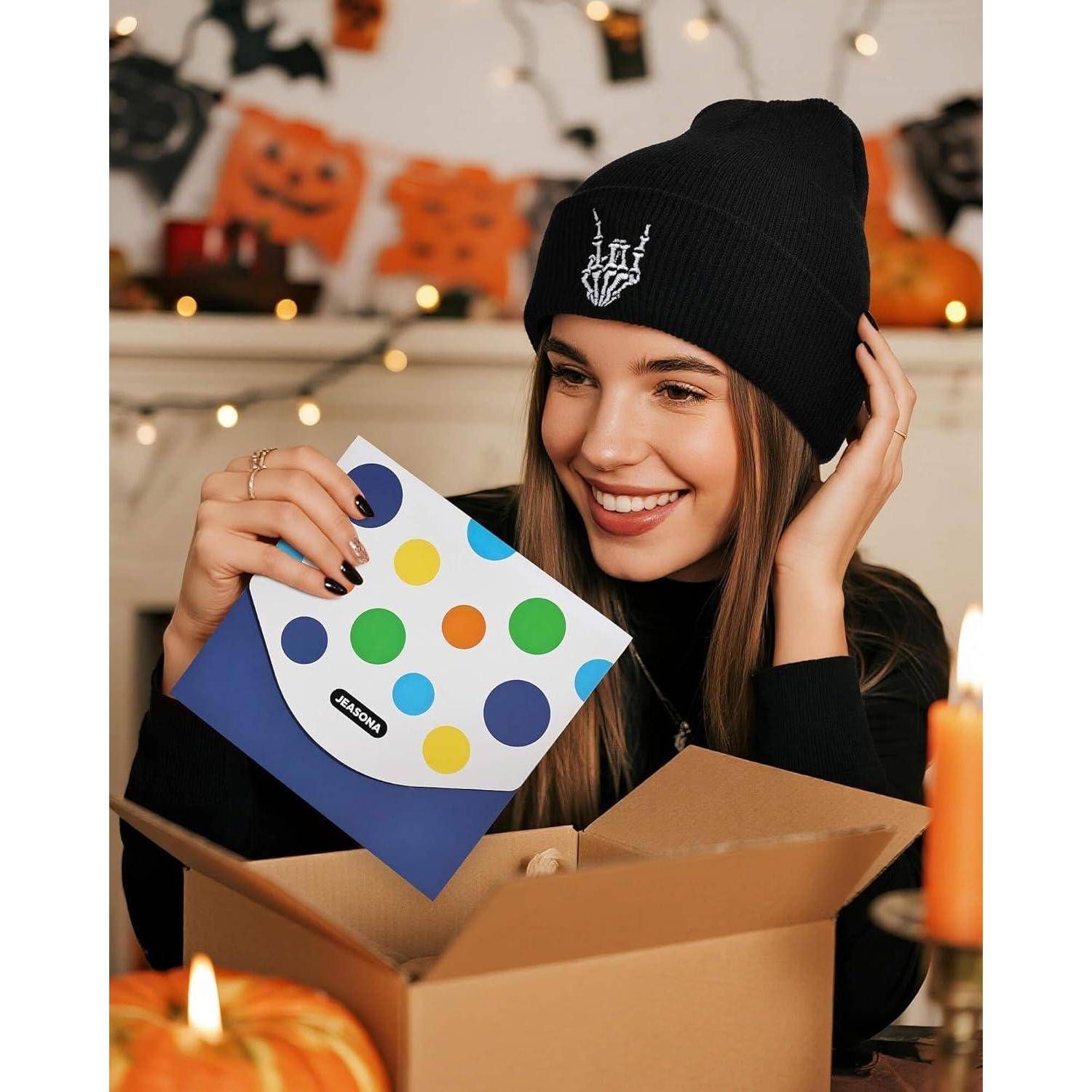 Eine Person mit einer schwarzen Beanie lächelt, während sie eine Kartonbox öffnet, die ein Paket mit buntem Polka-Dot-Design enthält. Im Hintergrund sind Halloween-Dekorationen zu sehen.