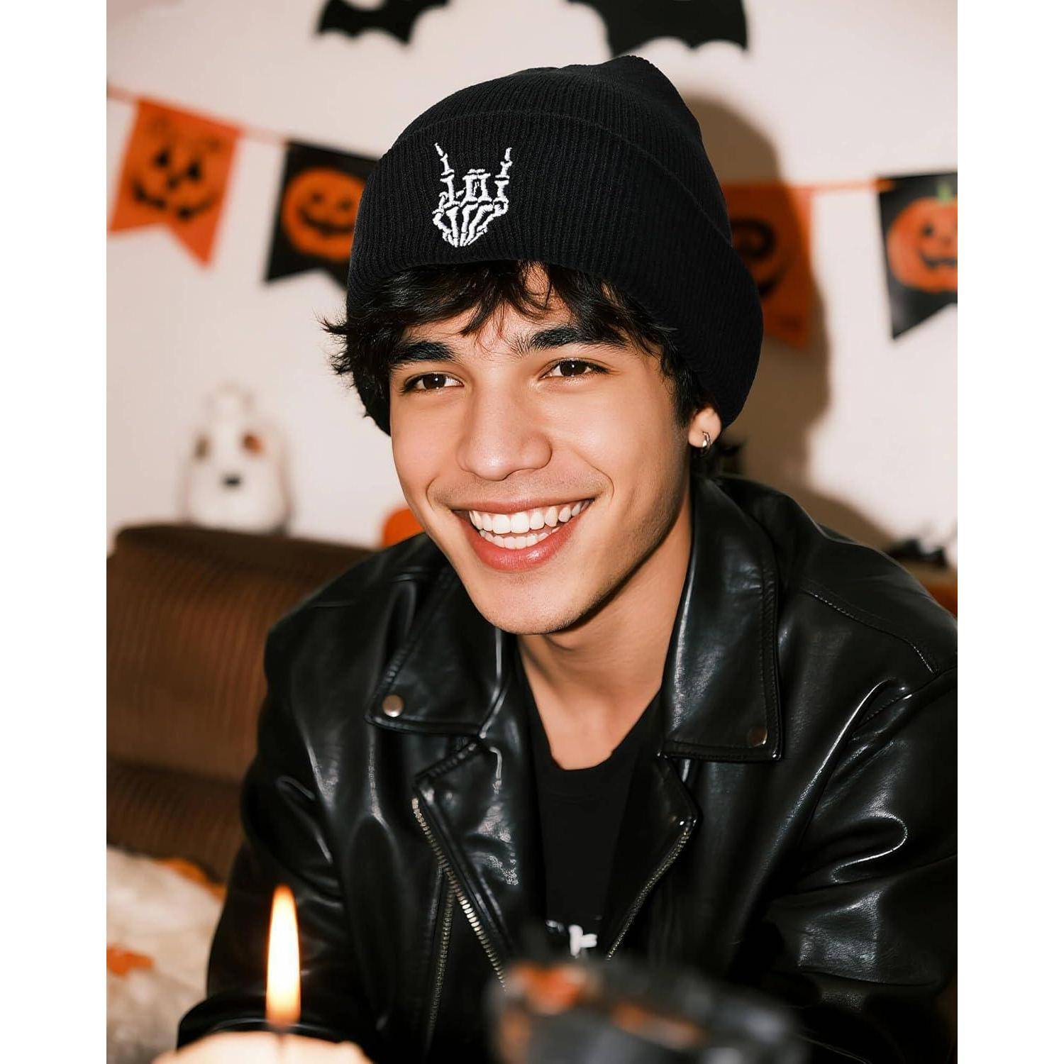 Eine Person, die lächelt und einen schwarzen Beanie sowie eine Lederjacke trägt, drinnen mit Halloween-Dekorationen im Hintergrund.