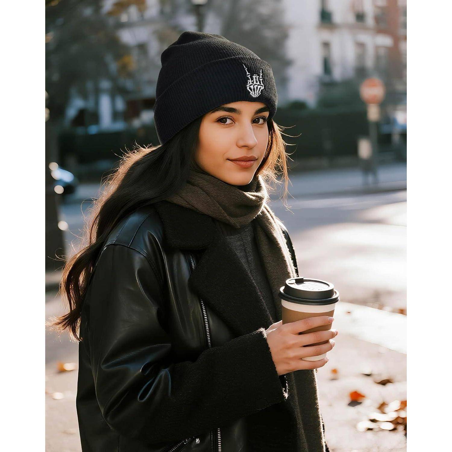 Eine Person steht im Freien, trägt eine schwarze Beanie-Mütze und eine Lederjacke und hält eine Kaffeetasse. Der Hintergrund zeigt eine verschwommene städtische Umgebung.