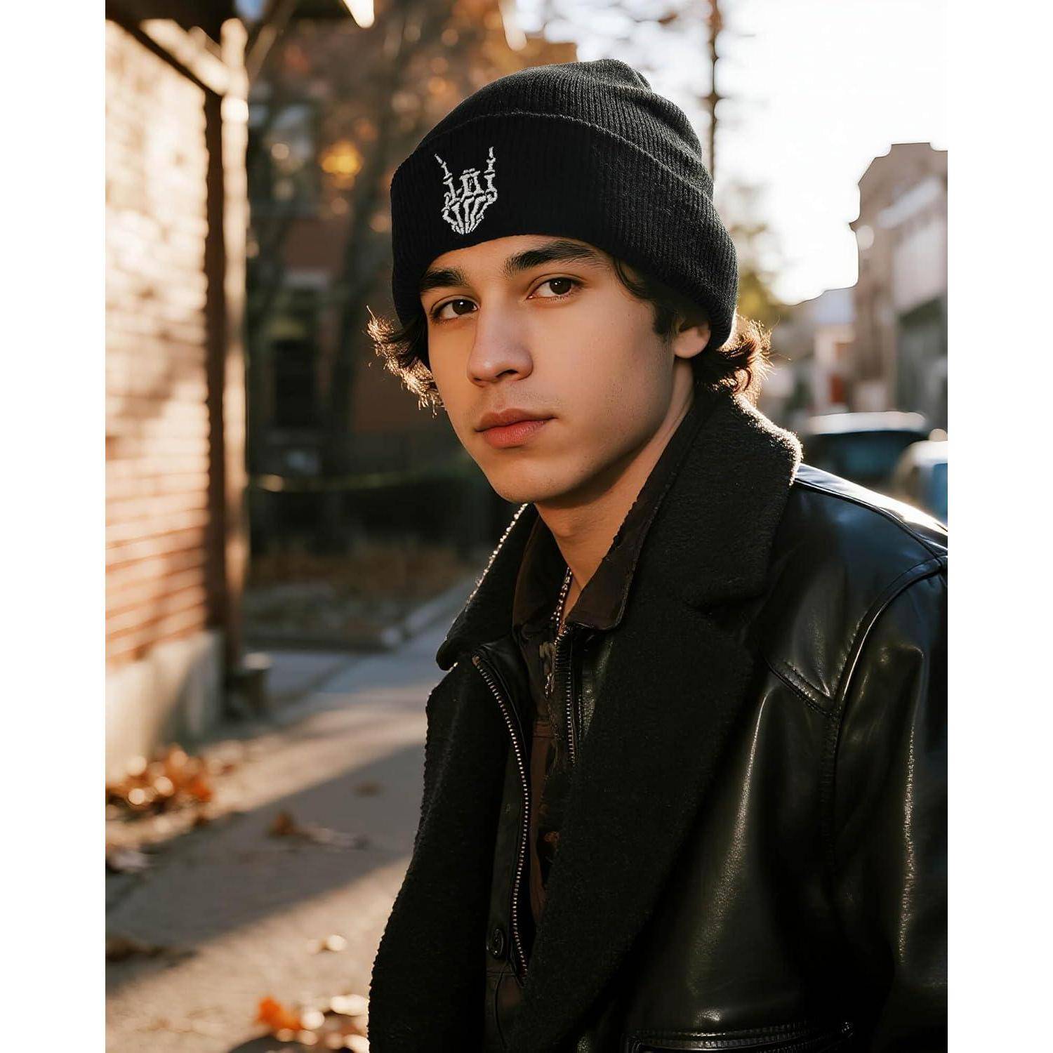 Eine Person mit einem schwarzen Beanie mit weißem Design und einer Lederjacke steht auf einer sonnenbeschienenen Straße, um sie herum verstreut Herbstblätter.