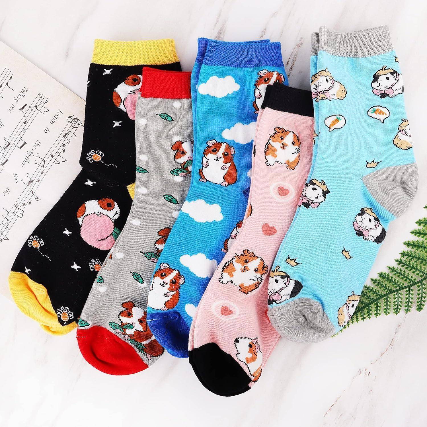 Fünf Paar farbenfrohe Socken mit verschiedenen Tiermotiven sind auf einer Marmoroberfläche ausgelegt. Ein Notenblatt und ein Farnblatt befinden sich in der Nähe.