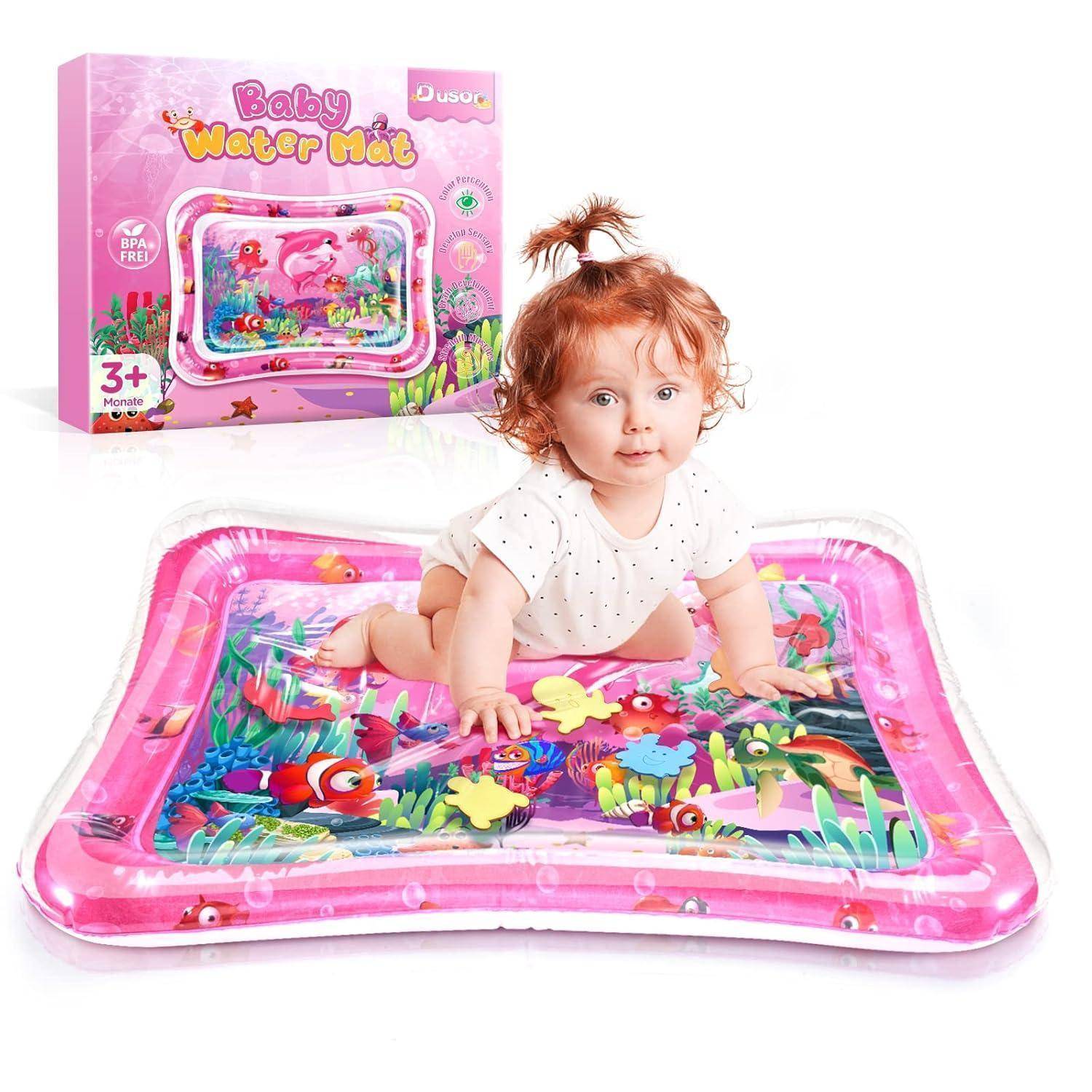 Ein Baby auf einer bunten Wassermatte mit aquatischen Designs, darunter Fische und Pflanzen. Verpackung im Hintergrund trägt die Aufschrift 