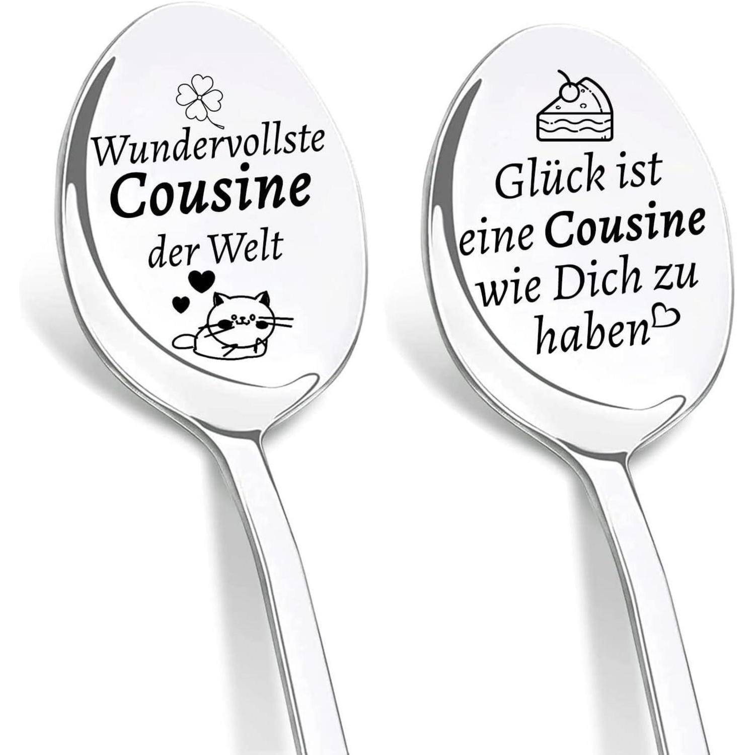 Zwei silberne Löffel mit deutschem Text. Linker Löffel: 'Wundervollste Cousine der Welt' mit einer Katzenzeichnung. Rechter Löffel: 'Glück ist eine Cousine wie Dich zu haben' mit einer Kuchenzeichnung.