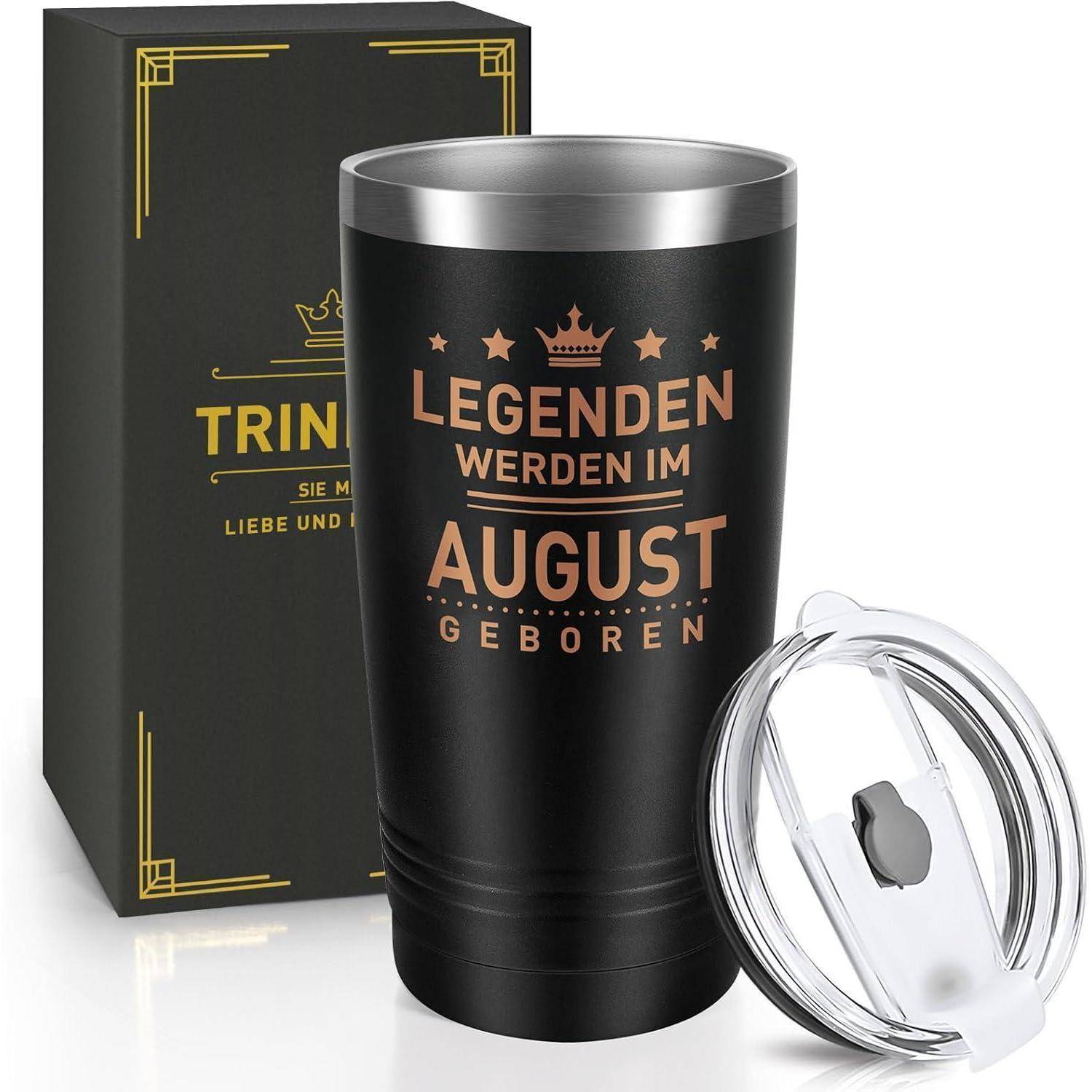 Eine schwarze Reisebecher mit dem Text 'Legenden werden im August geboren' neben einer schwarzen Box mit goldenen Akzenten und einem durchsichtigen Deckel.