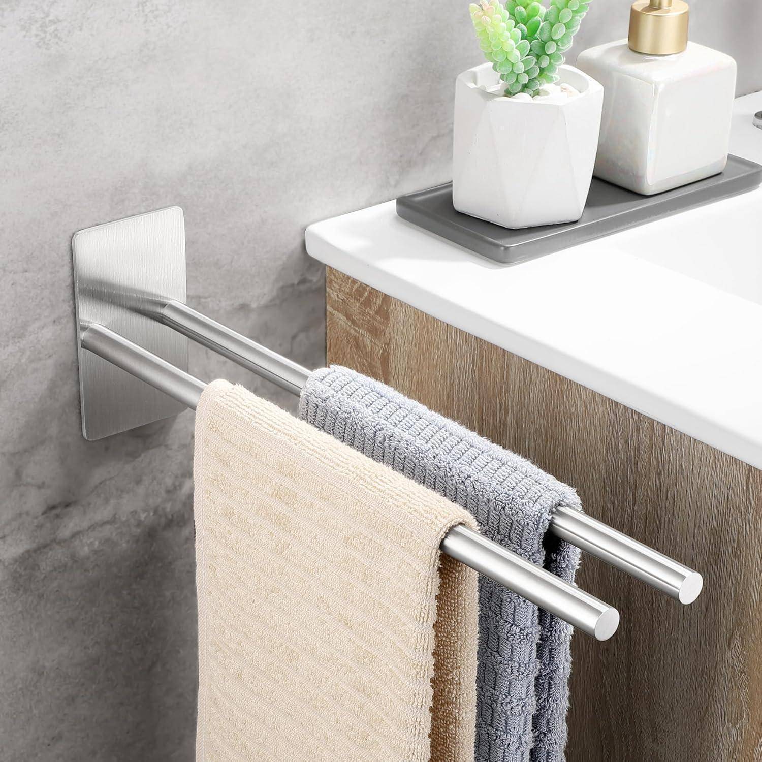 Ein Handtuchhalter, an einer Badezimmerwand montiert, hält zwei gefaltete Handtücher, einen in Beige und den anderen in Grau, unterhalb einer weißen Arbeitsplatte mit einer kleinen Pflanze.