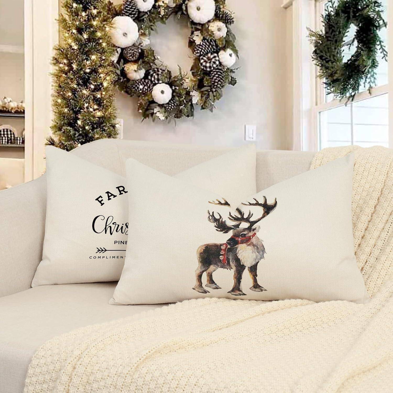 Ein gemütliches Wohnzimmer mit einem weißen Sofa, geschmückt mit weihnachtlich gestalteten Kissen und einer Decke. Ein Kranz und ein beleuchteter Weihnachtsbaum befinden sich im Hintergrund.