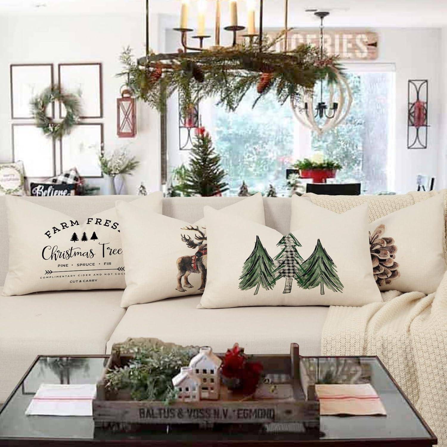 Wohnzimmer weihnachtlich dekoriert mit weißen Kissen auf dem Sofa mit festlichen Mustern, einem Mittelpunktstück auf dem Tisch und Grünzeug, das darüber hängt.