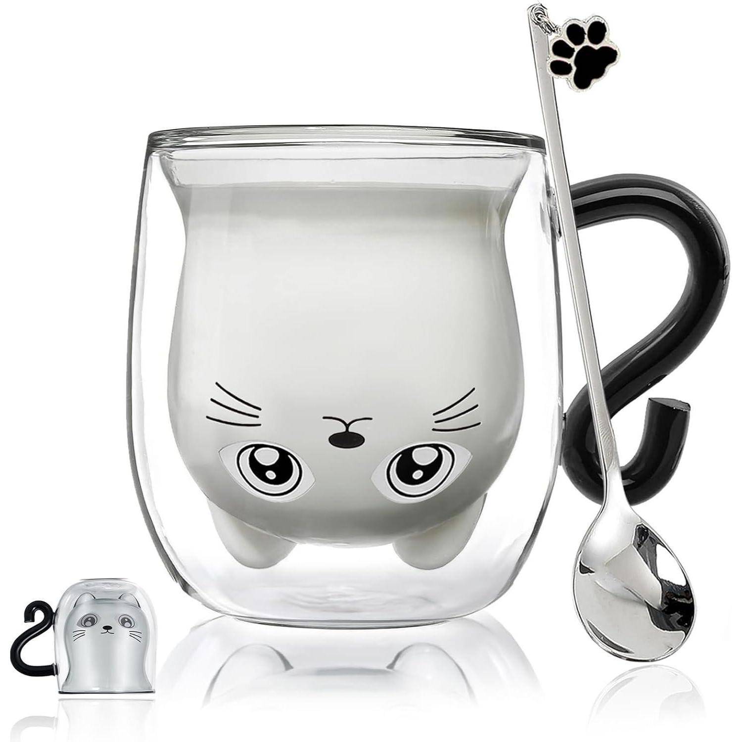 Eine transparente Tasse mit einer niedlichen, katzenförmigen Innenfigur, gefüllt mit Milch. Ein Löffel mit einem Pfotendruck und einem kleinen, katzenförmigen Deckel in der Nähe.
