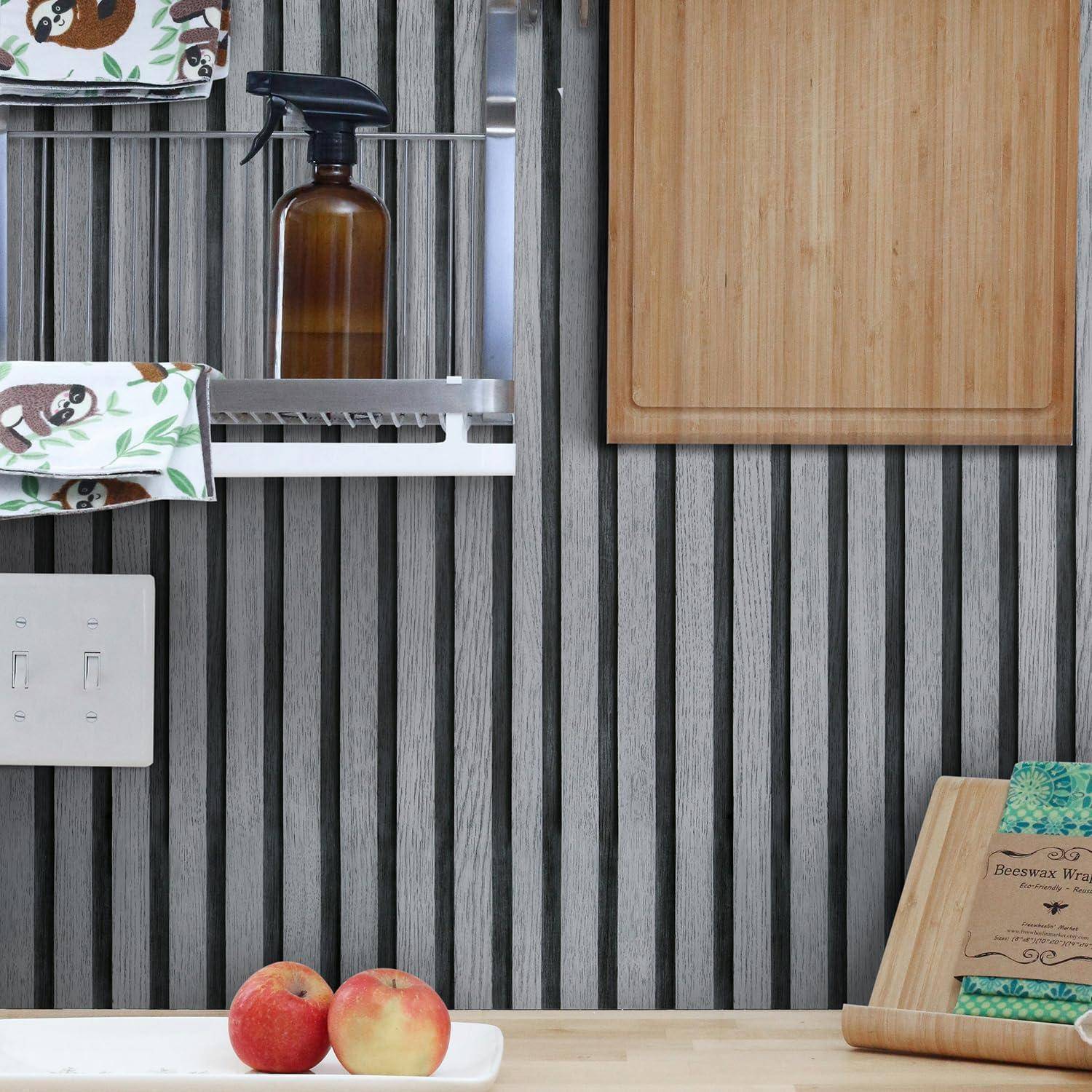Wandmontiertes Regal mit einer braunen Flasche, Holzschrank, Lichtschalter, Schneidebrett und zwei Äpfeln auf der Arbeitsplatte.