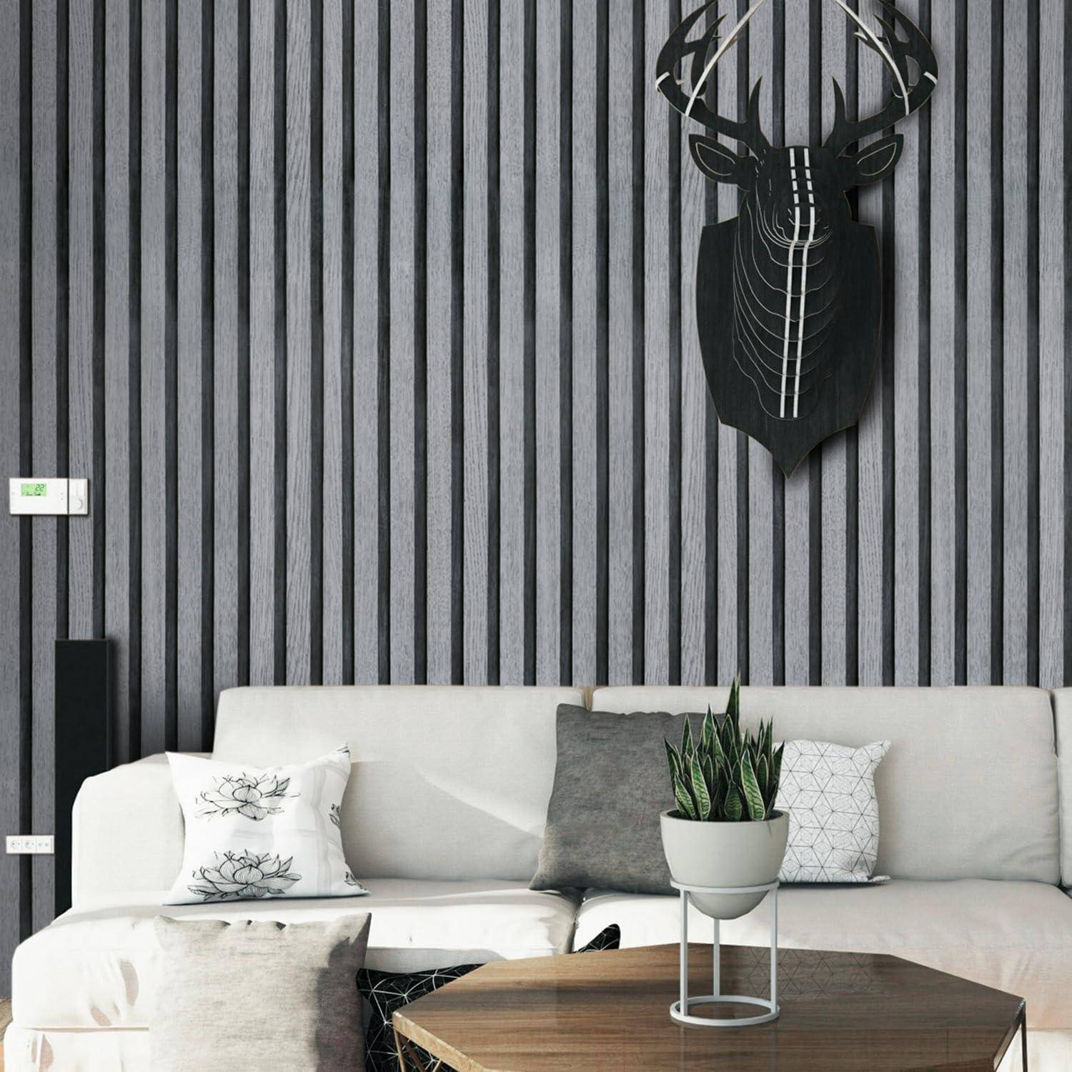 Ein modernes Wohnzimmer präsentiert ein graues Sofa mit gemusterten Kissen und einer Topfpflanze. Ein schwarzer Hirschkopf-Skulptur hängt darüber an einer gestreiften Wand.