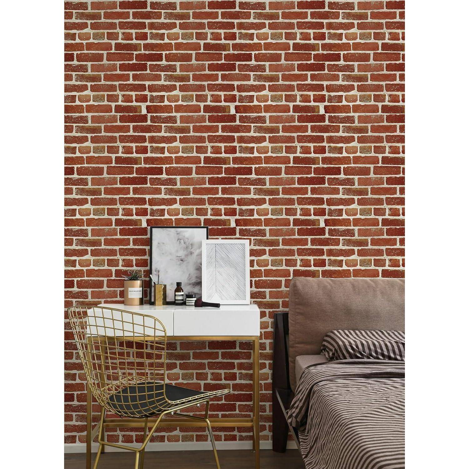 Ein Raum mit einer ziegelgemusterten Wand, einem Schreibtisch mit Büchern und Kunstwerken, einem Drahtsessel und einem Bett mit gestreifter Bettwäsche.