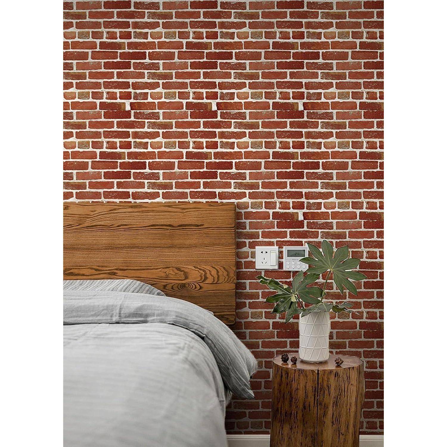 Eine Schlafzimmerszene mit einer rustikalen roten Ziegelwand, einem Holzkopfteil, grauer Bettwäsche und einer Topfpflanze auf einem kleinen, runden Holztisch.