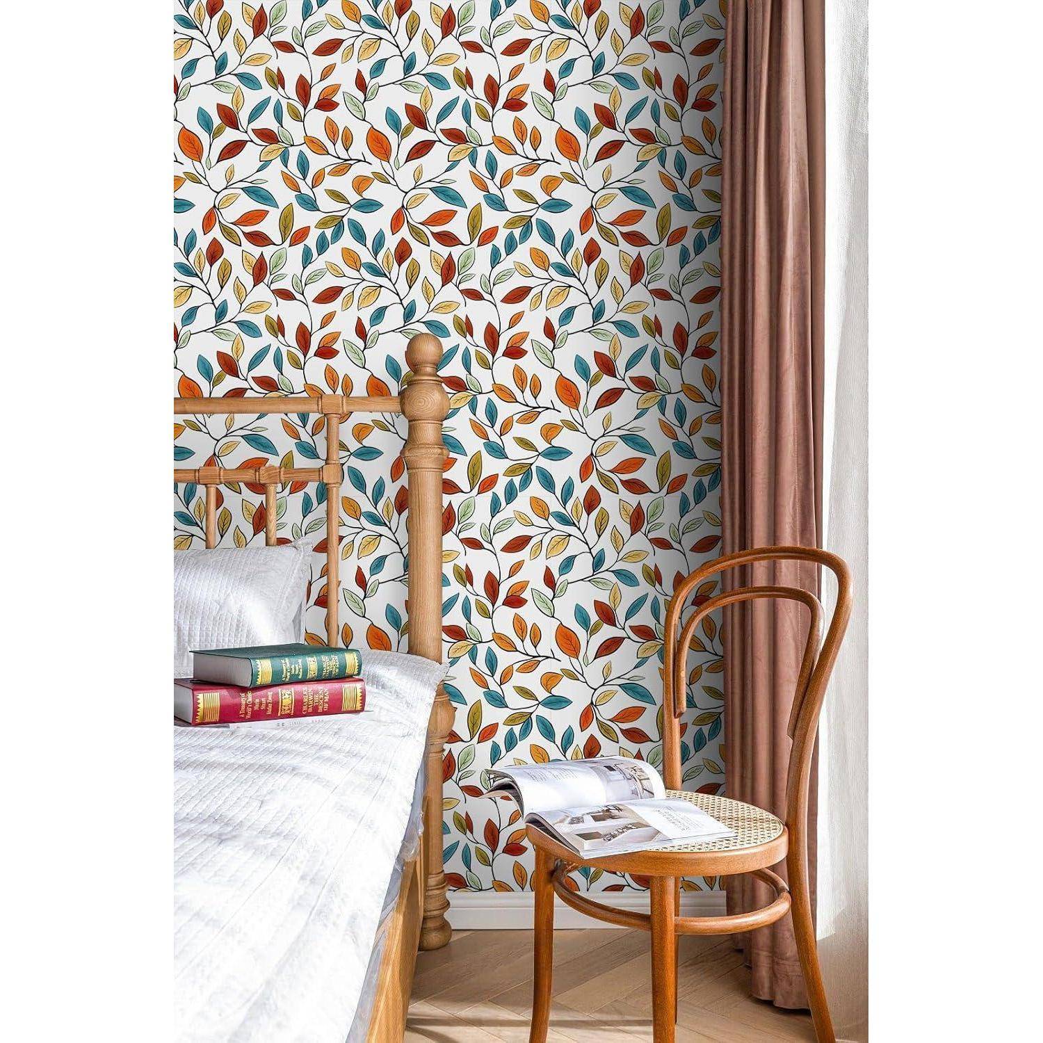 Eine Schlafzimmerecke mit einem Holzbett, gemusterten Bettwäsche, einem Stapel Bücher, einem braunen Stuhl und Tapeten mit einem Herbstblätter-Design.
