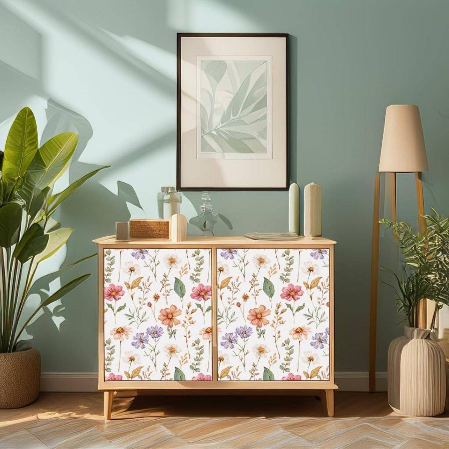 Ein lichtdurchfluteter Raum mit einem blumengemusterten Schrank, Pflanzen und einem gerahmten Blatt-Kunstwerk an einer blauen Wand, der einen ruhigen, stilvollen Raum schafft.