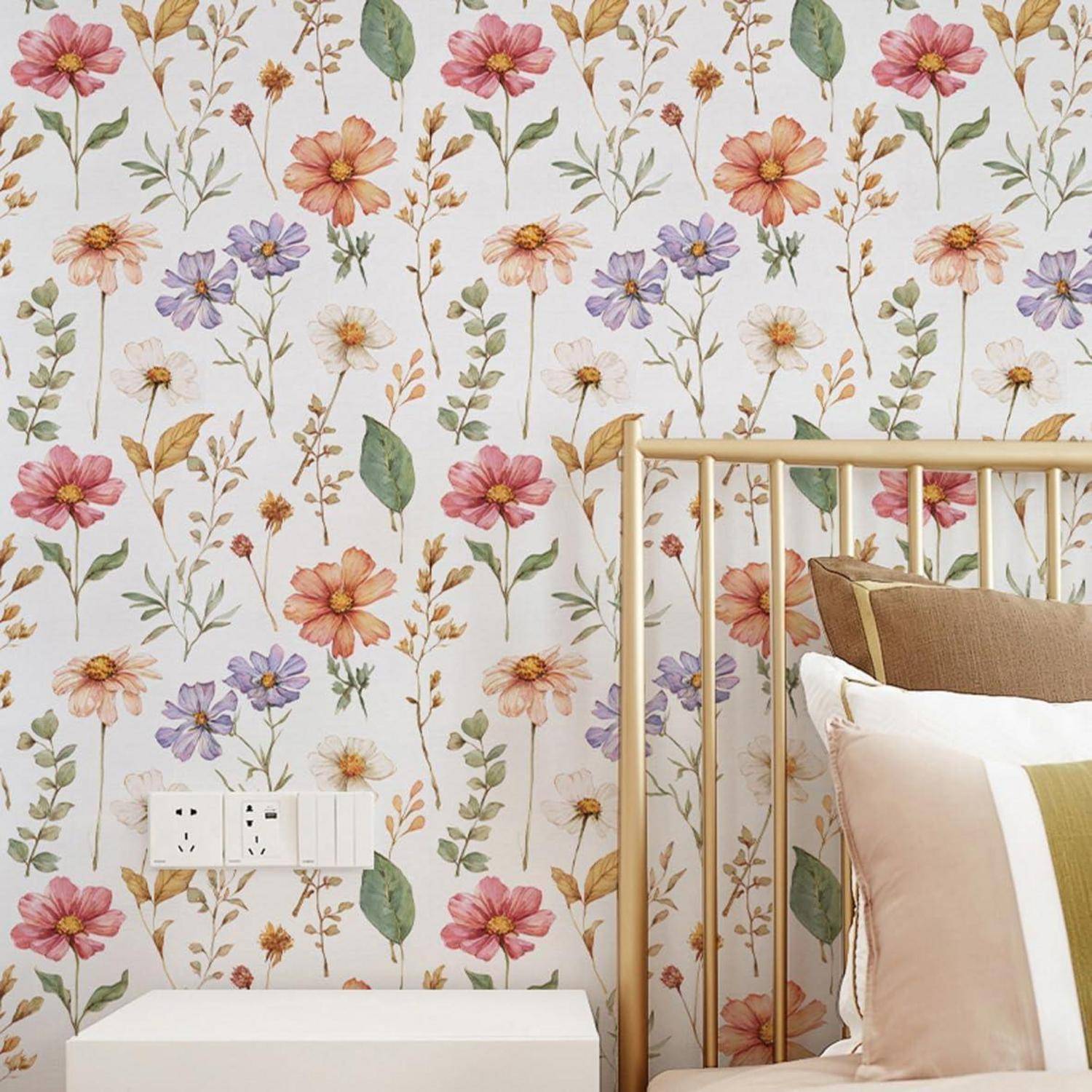 Eine gemütliche Schlafzimmerecke mit Blumentapete, einem Holzbett mit beigen und braunen Kissen und einem weißen Nachttisch mit Steckdosen.