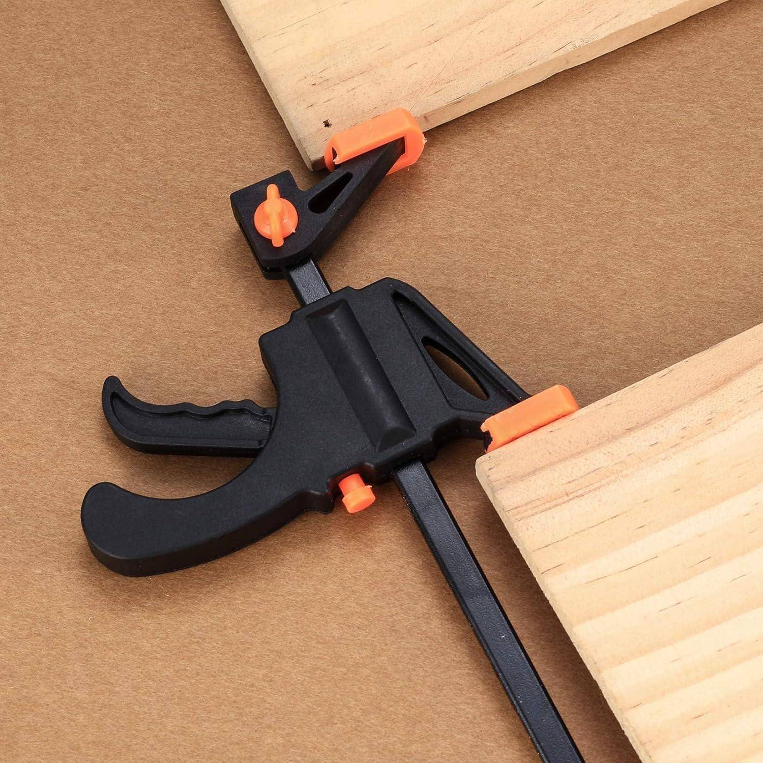 Eine Nahaufnahme einer schwarzen und orangefarbenen Schraubzwinge, die zwei Holzbretter auf einer braunen Oberfläche zusammenhält.